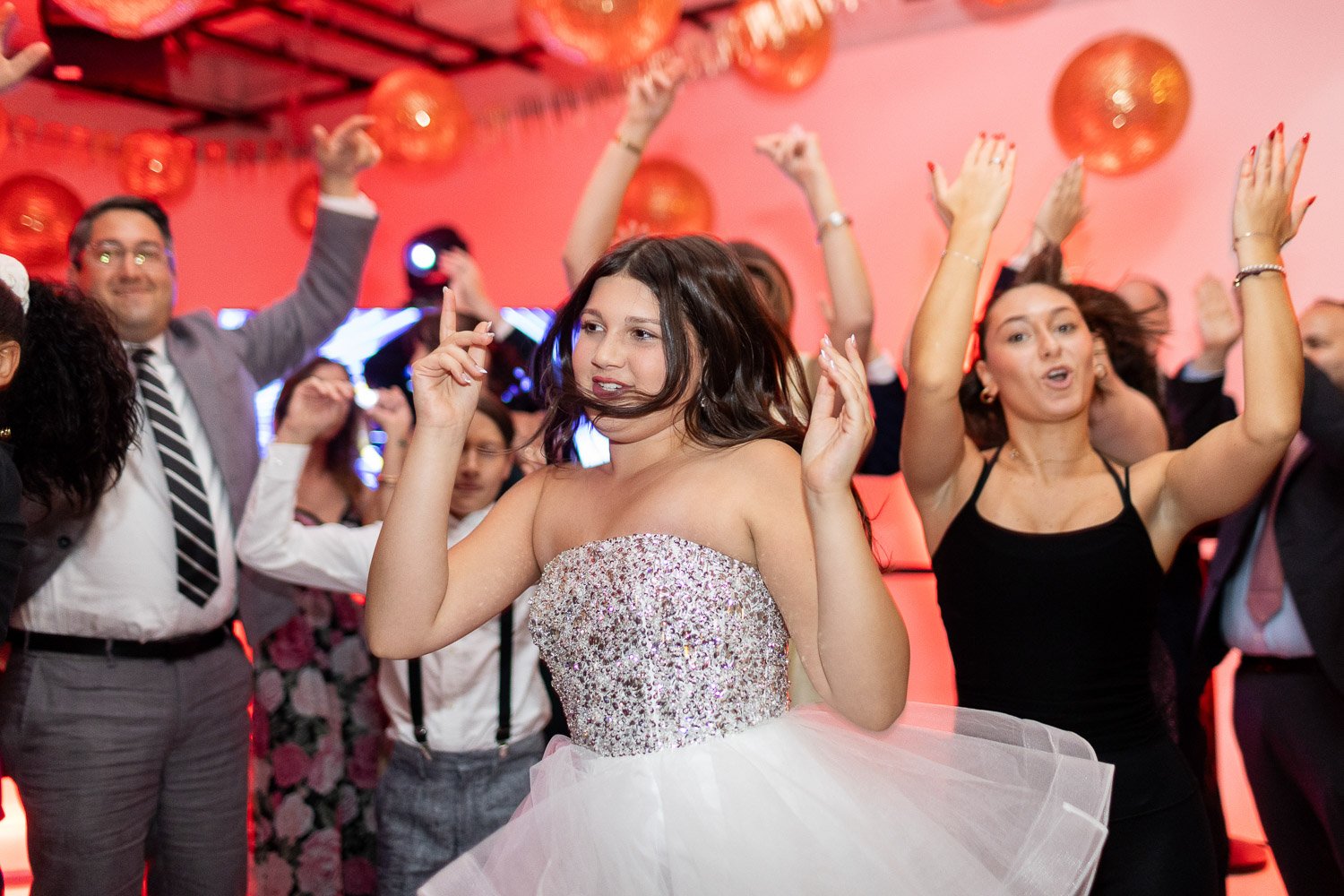People dancing and celebrating at a Bat Mitzvah with pink and red decorations.