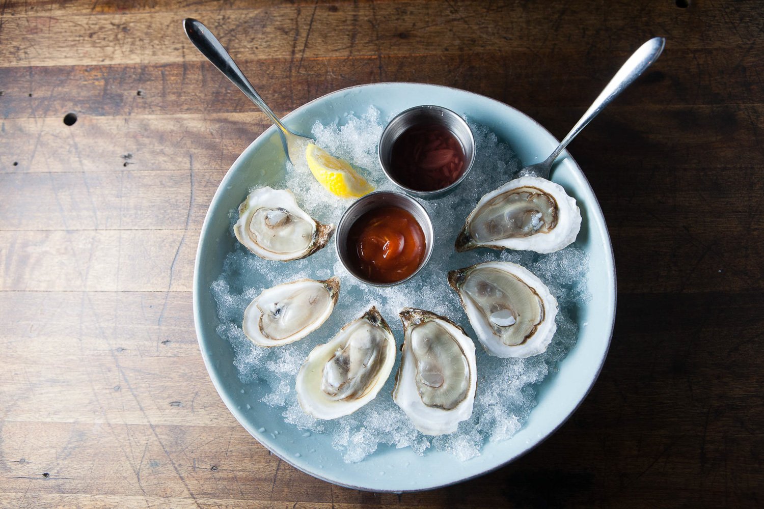 Plate of fresh oysters on ice with lemon wedge and two sauces