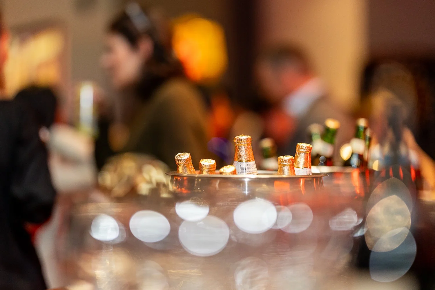 Bottles of beer on a table at a social gathering in a blurred indoor setting.