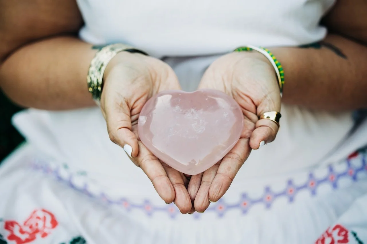 Person holding a heart-shaped pink crystal in both hands.