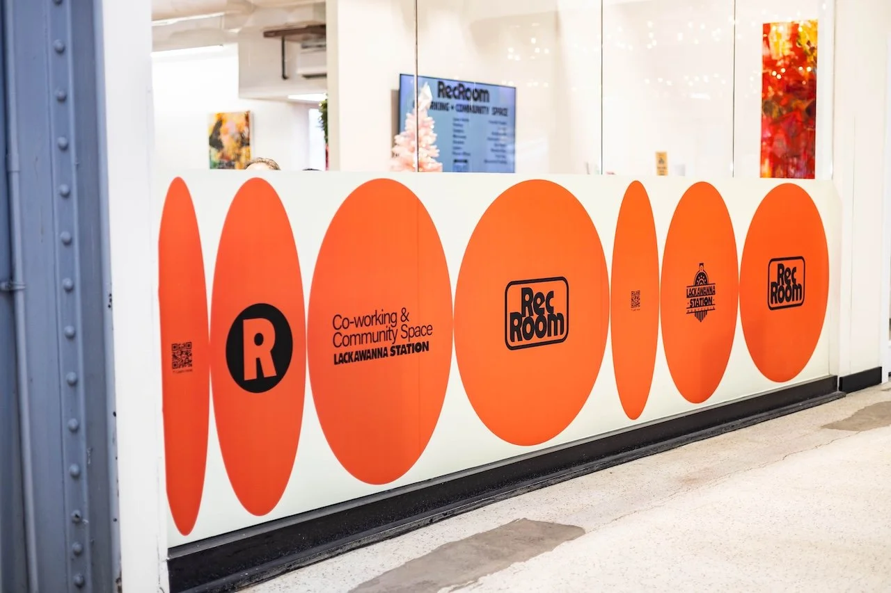 Sign for a co-working and community space called Rec Room at Lackawanna Station, featuring large orange circles with black and white text and logos.