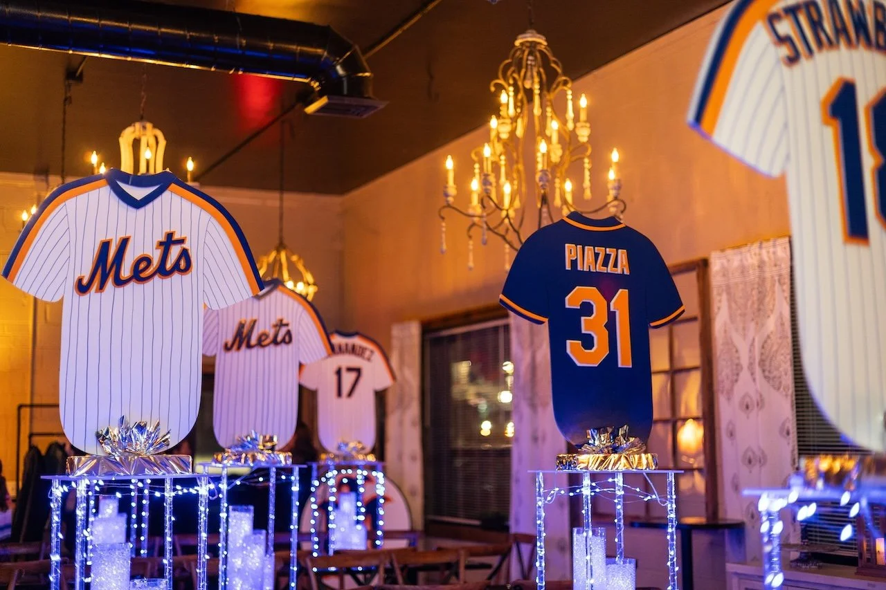 Several New York Mets baseball jerseys displayed on stands with decorative lights in a warmly lit room.