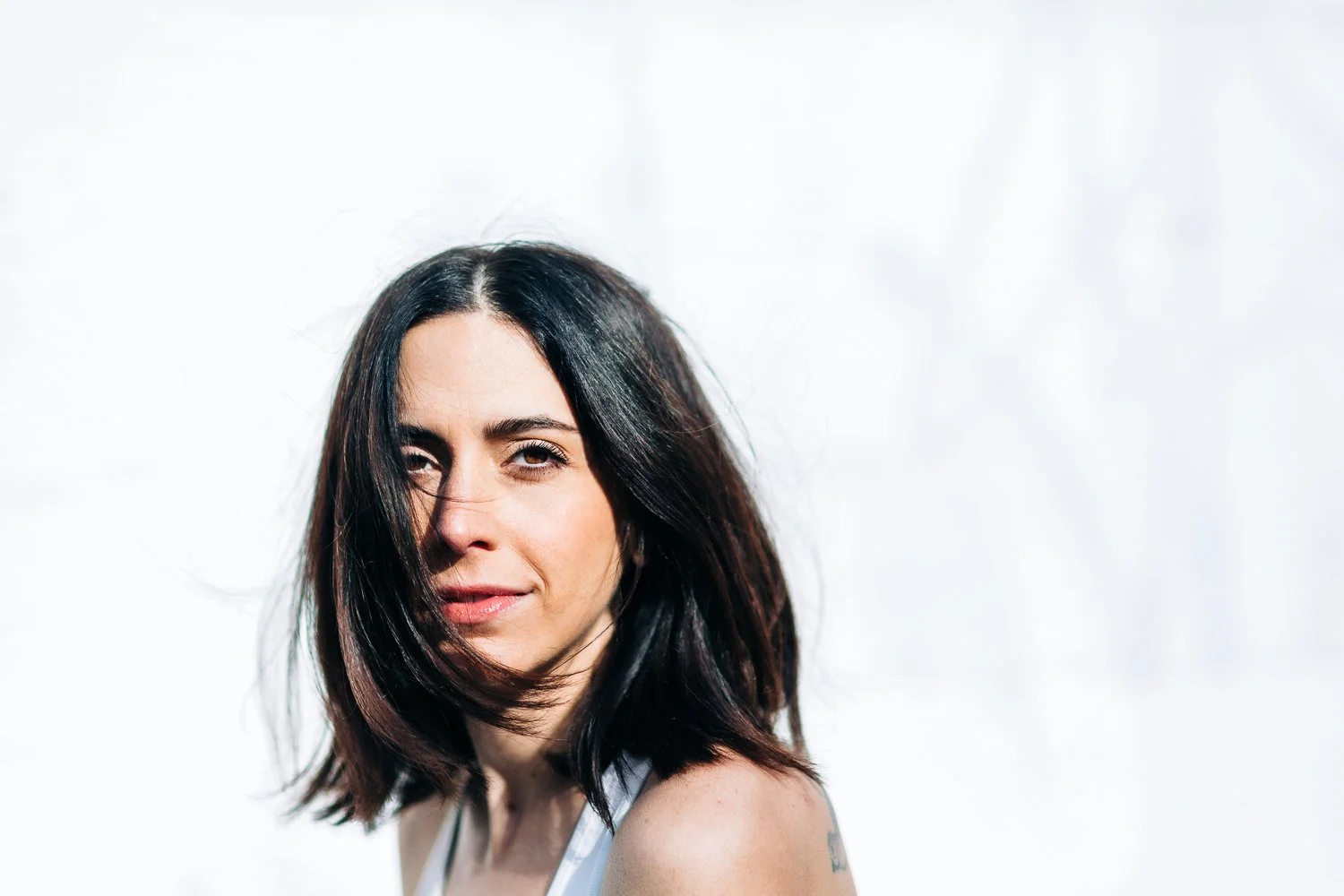 A woman with shoulder-length dark hair and light skin looking at the camera against a bright background.