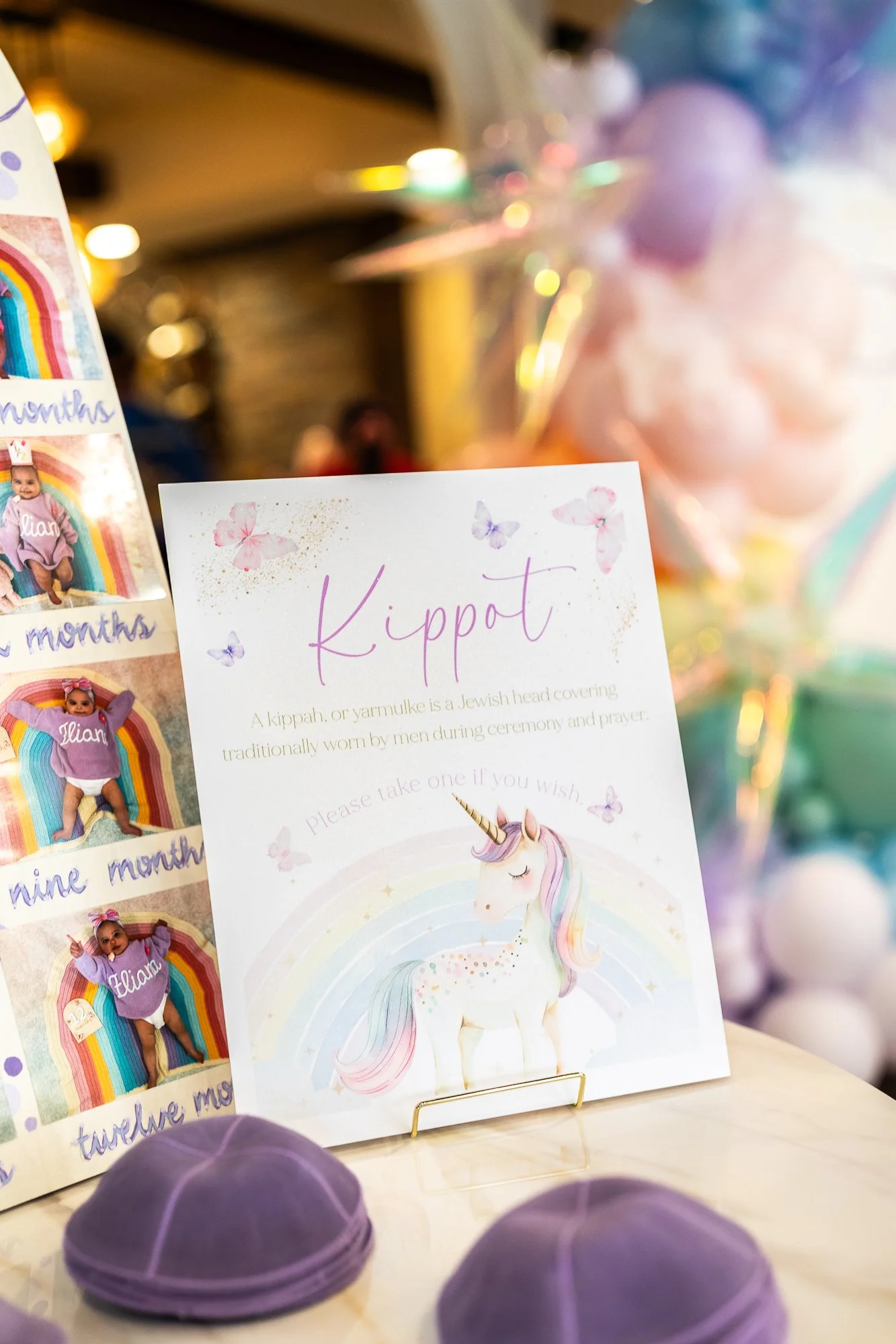 A display about Jewish head coverings called kippot or yarmulkes, featuring a card with a unicorn illustration and information, with purple yarmulkes in the foreground and a blurred background with colorful, shiny decorations.