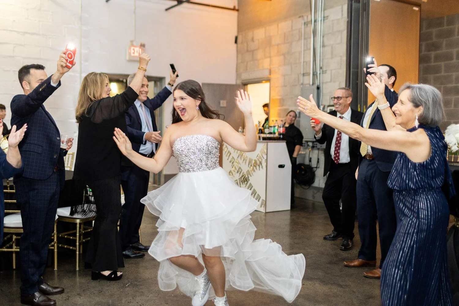 A bride dancing with guests at her wedding reception, surrounded by people taking photos and celebrating.