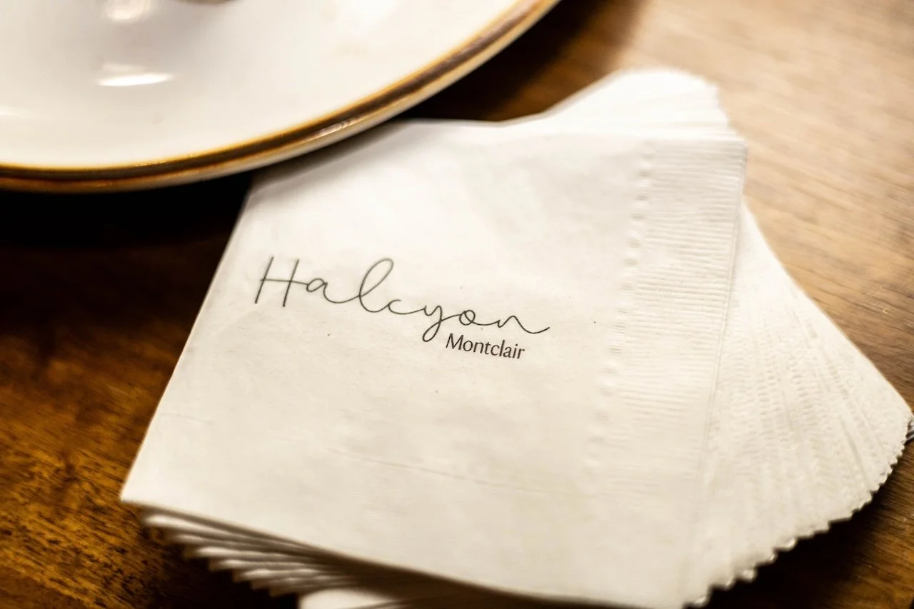 Napkin with the name 'Halcyon Montclair' written on it, placed on a wooden table next to a white plate.