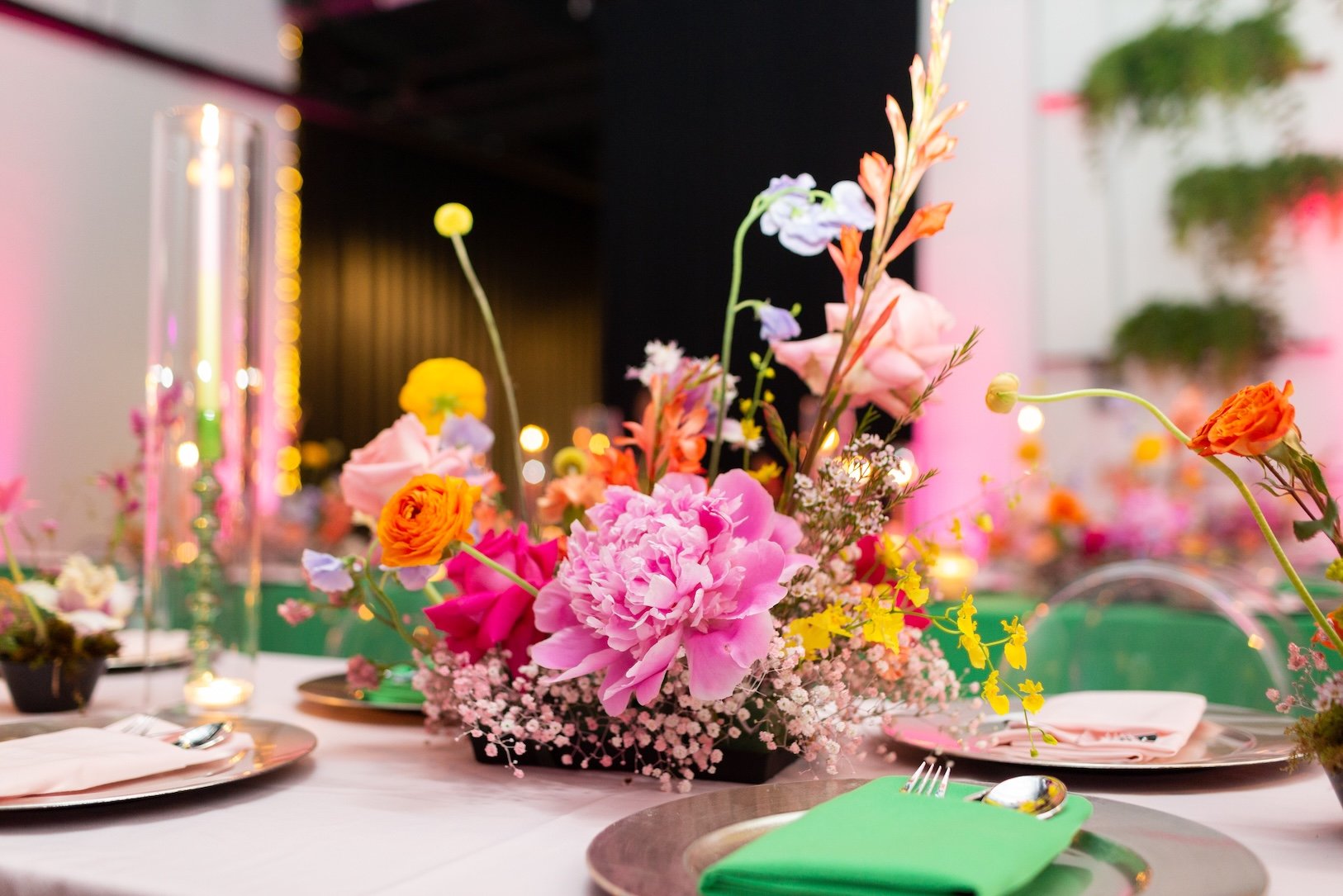 A close-up of a floral centerpiece with pink, orange, purple, and yellow flowers on a decorated table at a celebration event.