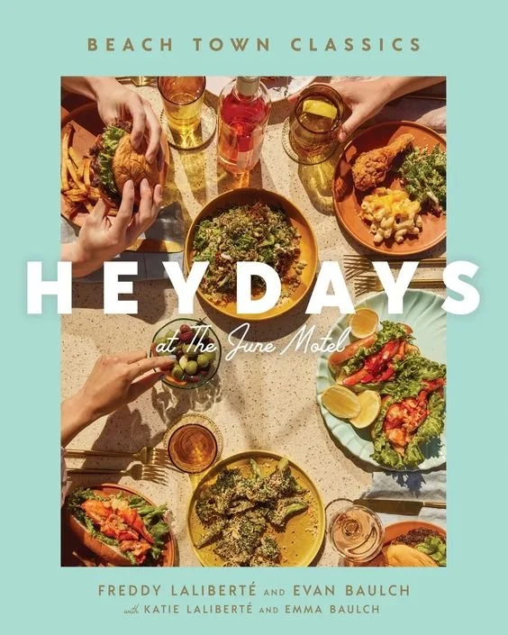HEYDAYS RESTAURANT COOKBOOK at The June Motel. A styled photographed table filled with various dishes, drinks, and hands holding food, set for a meal.