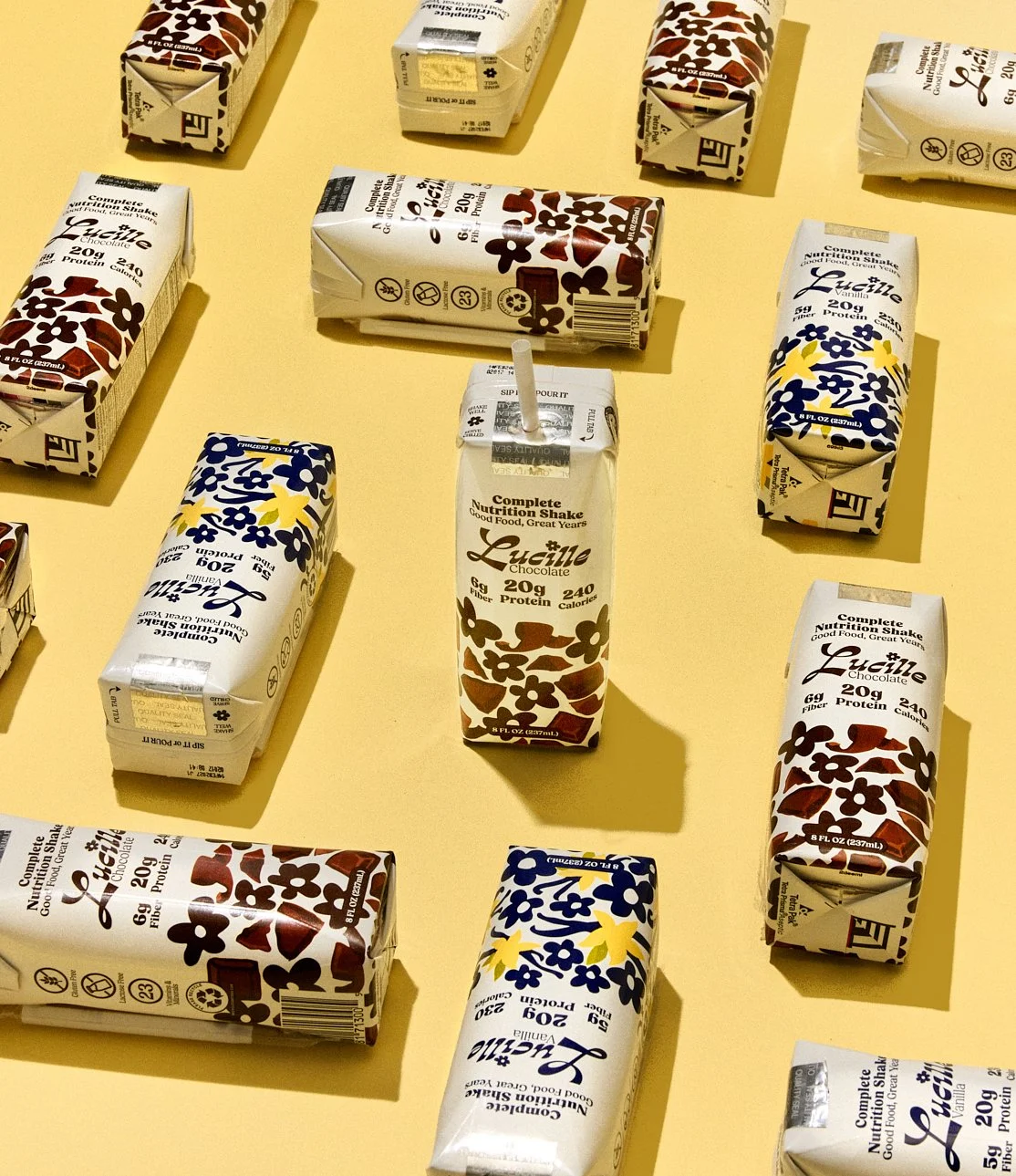 Still life creative photography prop styled by rayna marlee for Lucille. Multiple flavored plant-based nutrition shake cartons arranged on a yellow background, including chocolate and vanilla flavors.