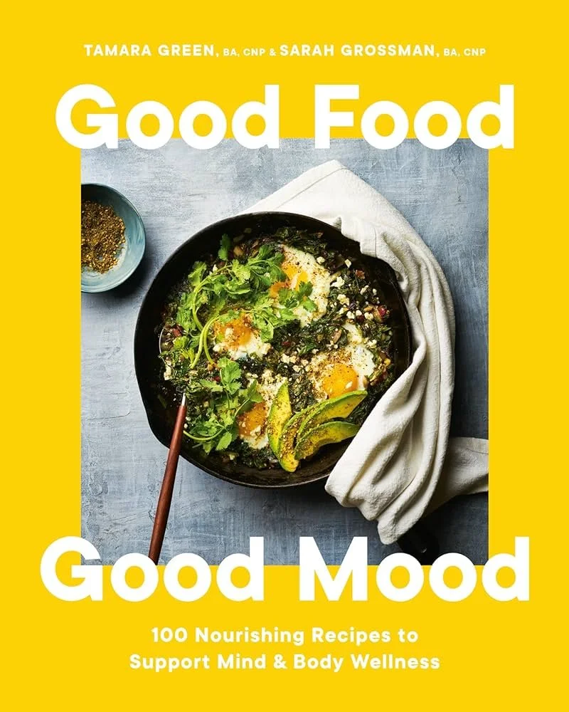 Photography cover of a cookbook titled 'Good Food, Good Mood' with a photo of a bowl containing eggs, avocado, greens, and grains, placed on a table with a small bowl of mustard or dressing beside it. Prop styled by rayna marlee.