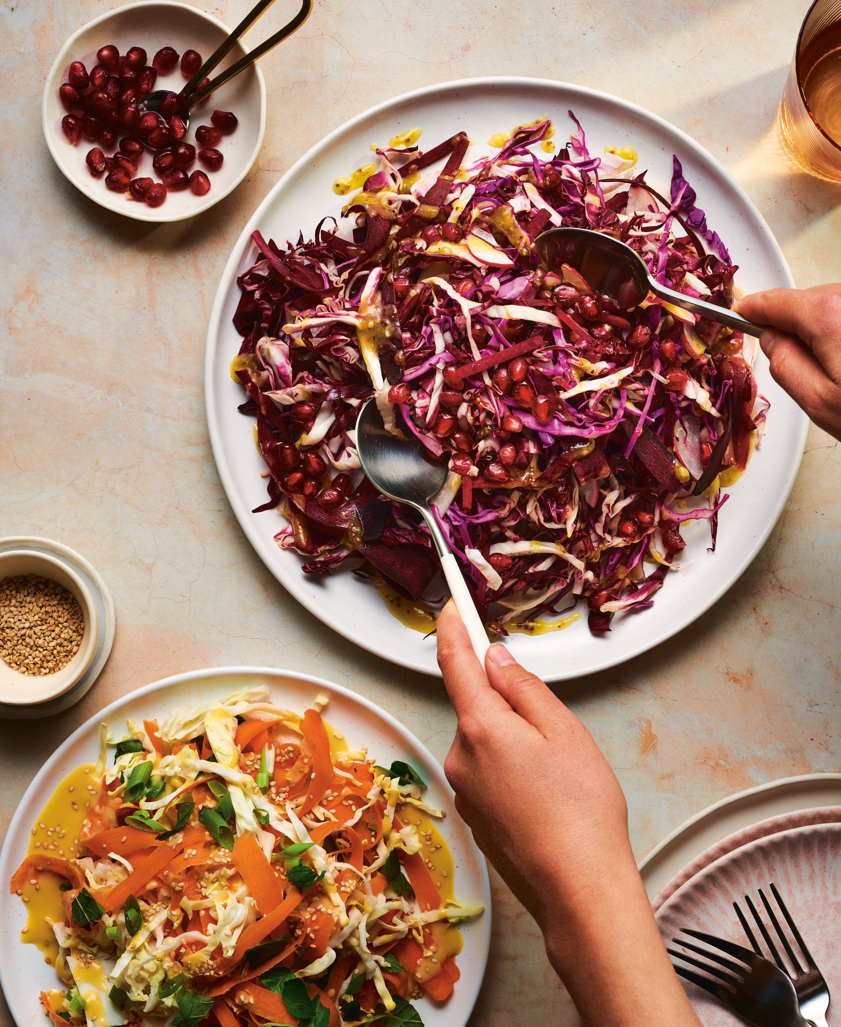 Photography cover of a cookbook titled 'Good Food, Good Mood' with two people serving themselves a salad with red cabbage, pomegranate seeds, and dressing in a large white bowl. A separate plate of carrot, cabbage, and green onions .