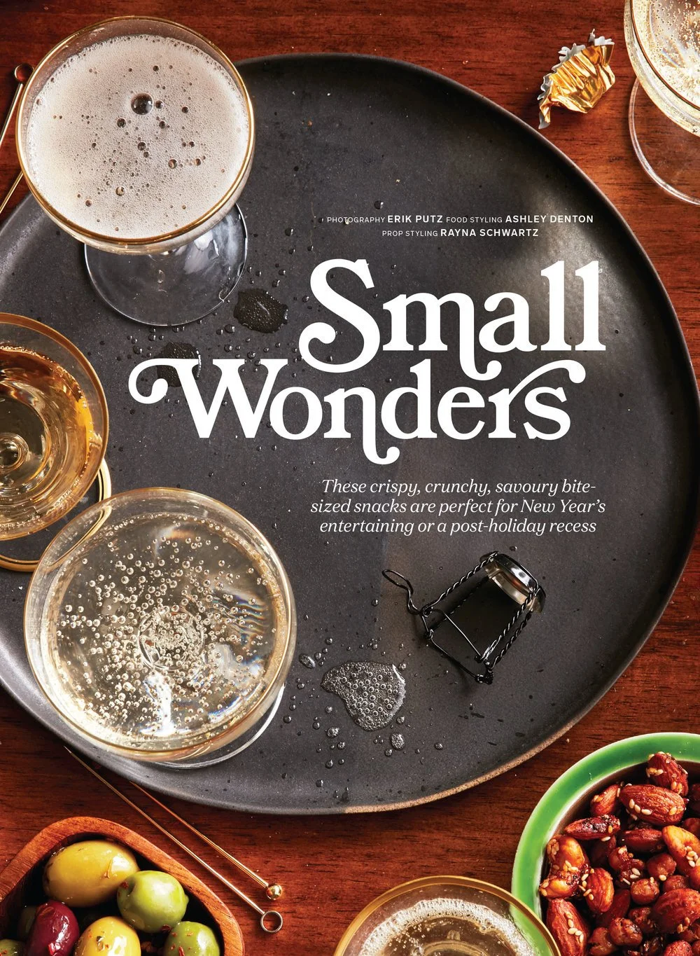 Chatelaine Magazine editorial prop styled by rayna marlee. a black tray with glasses of beer, bowls of nuts and snacks, and a small bottle opener on a wooden table.