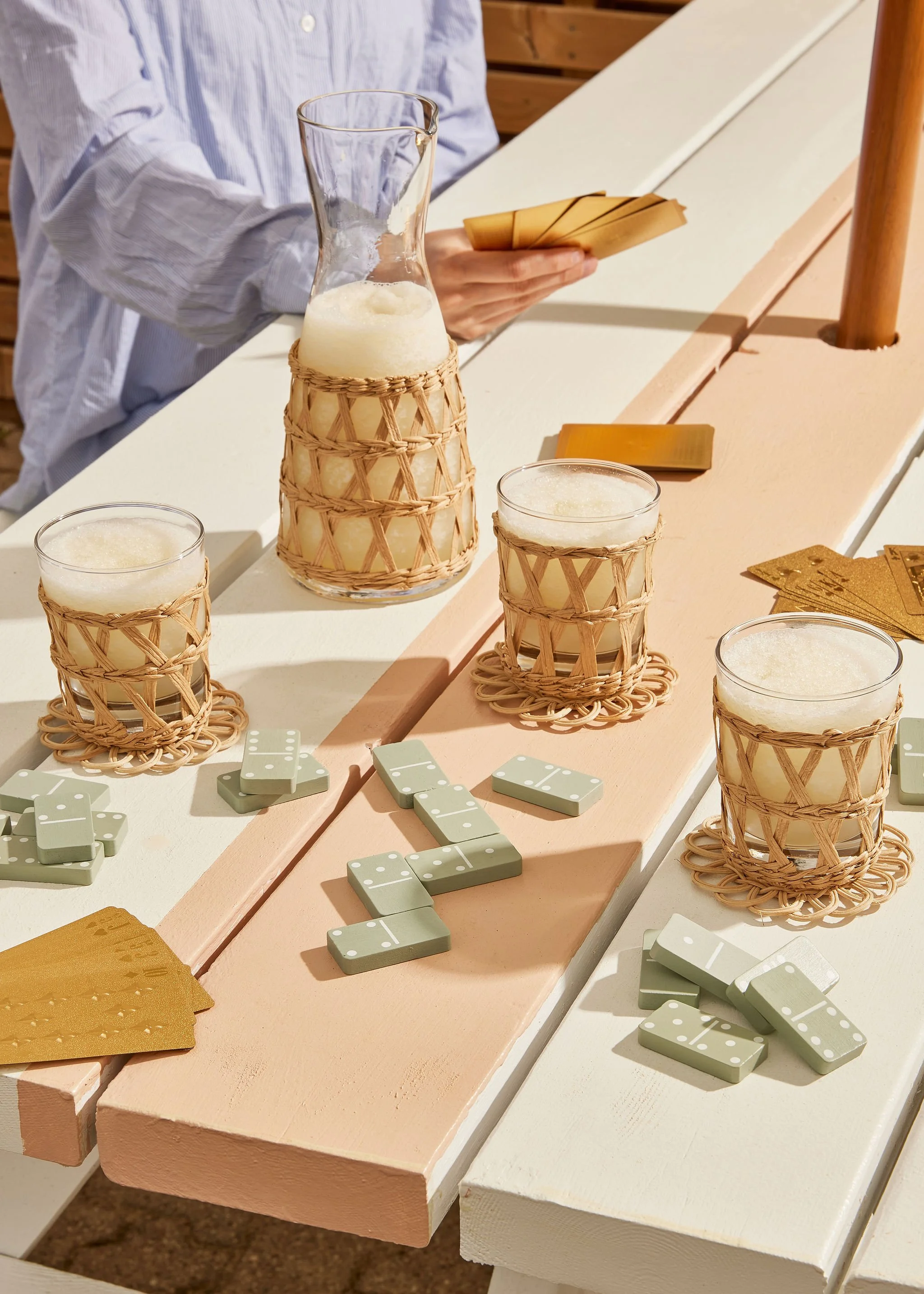 Still life creative photography prop styled and art directed by rayna marlee. People playing dominoes at a table with glasses of drinks and playing cards, outdoors on a sunny day.