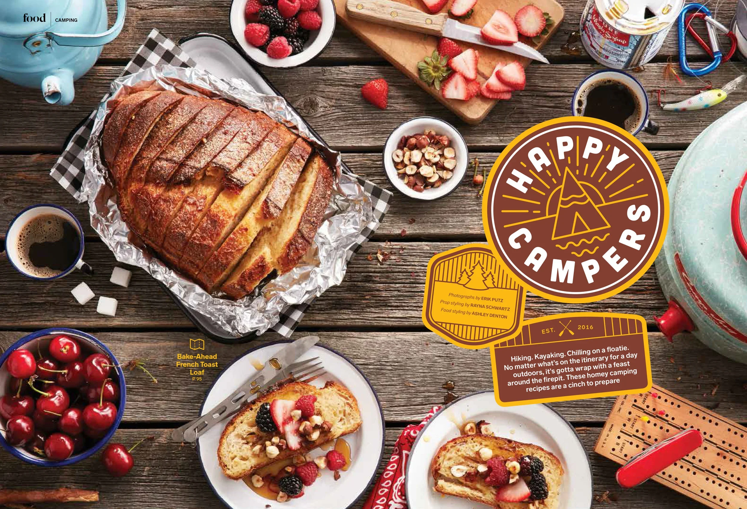 A picnic table with various foods and camping gear, including a loaf of French toast with powdered sugar, strawberries, blackberries, and raspberries, cups of coffee, cherries in a bowl, a teapot, a jar of cream, a bowl of mixed nuts, and a slice of 