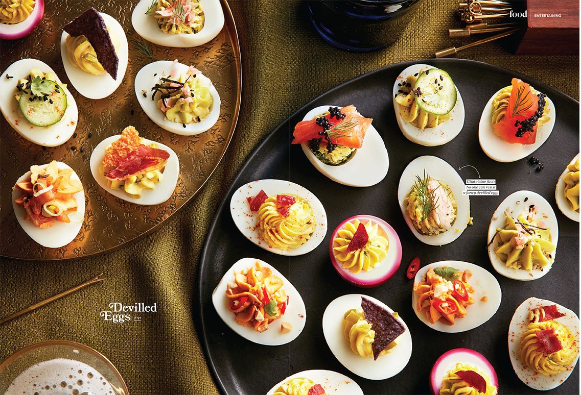 Chatelaine Magazine editorial prop styled by rayna marlee. Deviled eggs garnished with various toppings and fillings, arranged on two serving trays and a small plate on a green tablecloth.