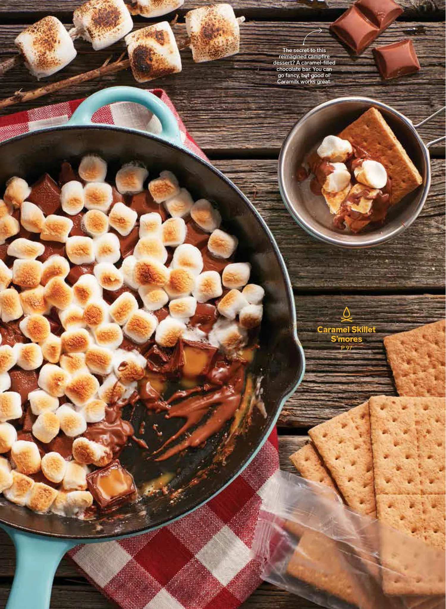 Chatelaine Magazine, styled by rayna marlee. S'mores dessert in a baking dish topped with toasted marshmallows, surrounded by graham crackers, a bowl with a graham cracker, chocolate,on a rustic wooden surface.