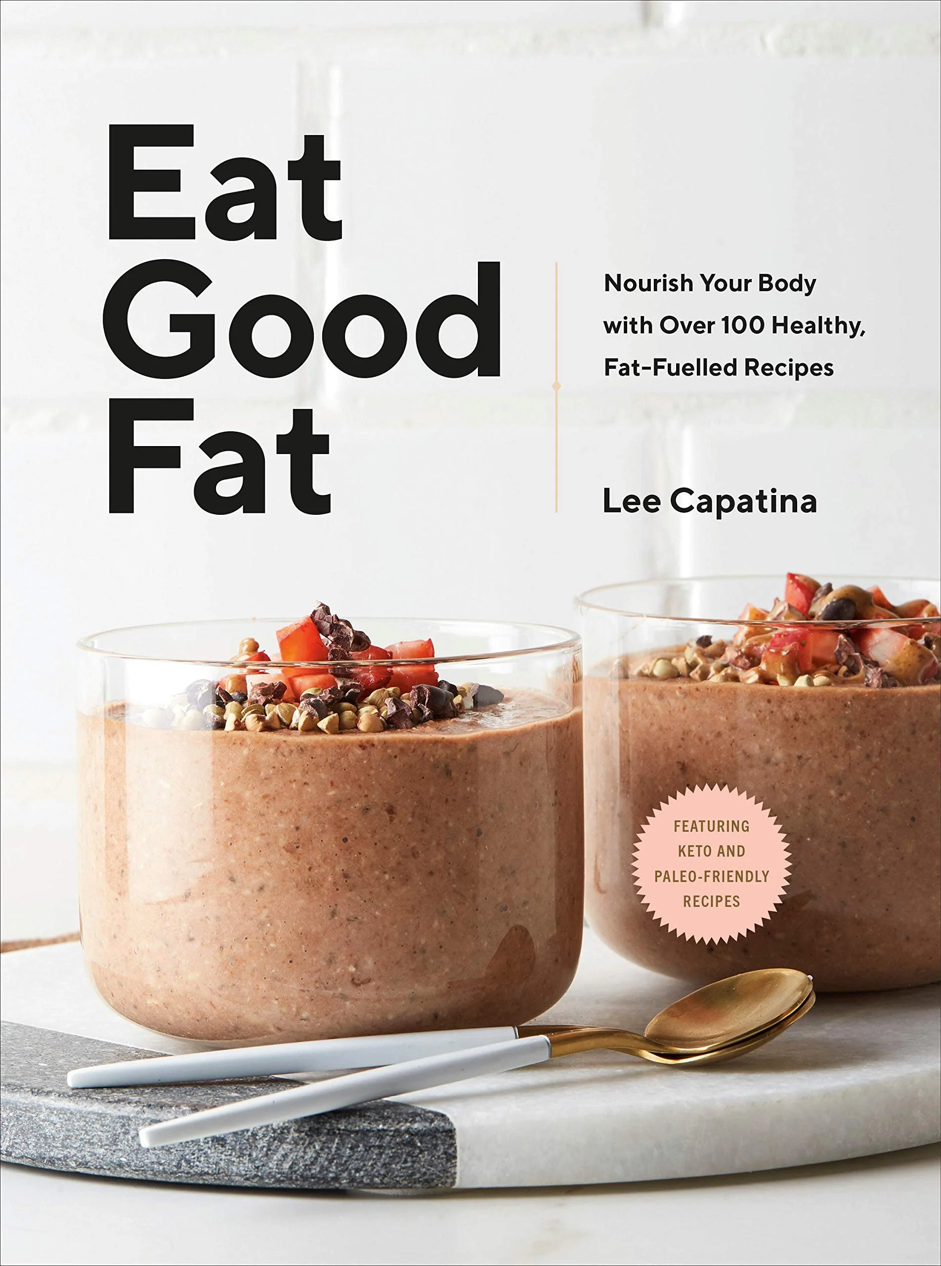 Cover of a cookbook titled "Eat Good Fat" art direction and prop styled by rayna marlee. featuring two glasses of chocolate smoothie topped with chopped fruit and seeds, with a spoon and a plate in the foreground.