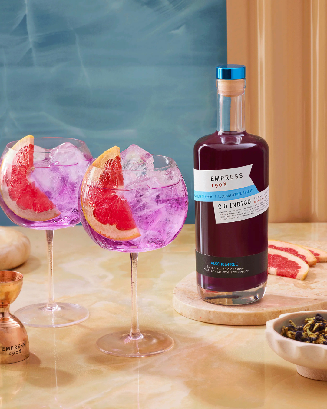 Drink photography prop styled and art directed by rayna marlee. Two glasses of pink grapefruit cocktail with ice and grapefruit slices, a bottle of alcohol-free spirit labeled Empress 1908 0.0 Indigo gin