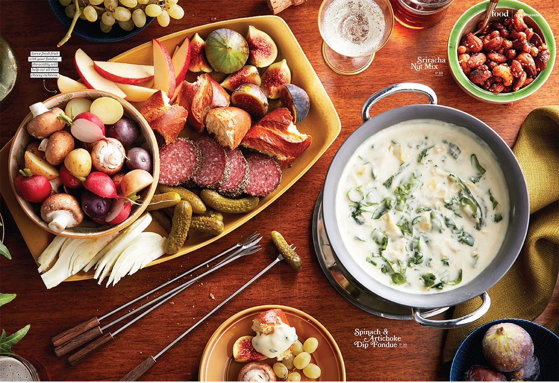 Chatelaine Magazine editorial props A table set with a variety of foods including a large cheese and fruit platter, a bowl of mixed nuts, a bowl of colorful radishes and mushrooms, a small plate of fruit and cheese slices and glasses of beverages.