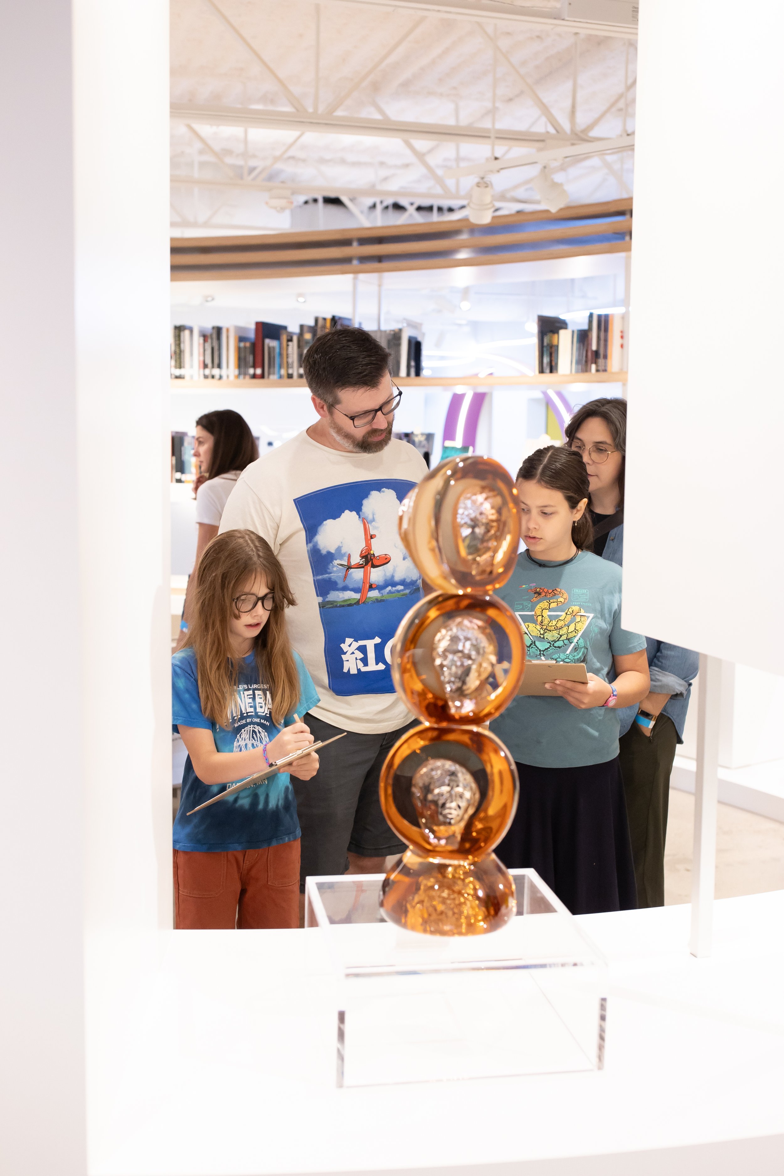 A group of adults and young people gather around a sculpture.
