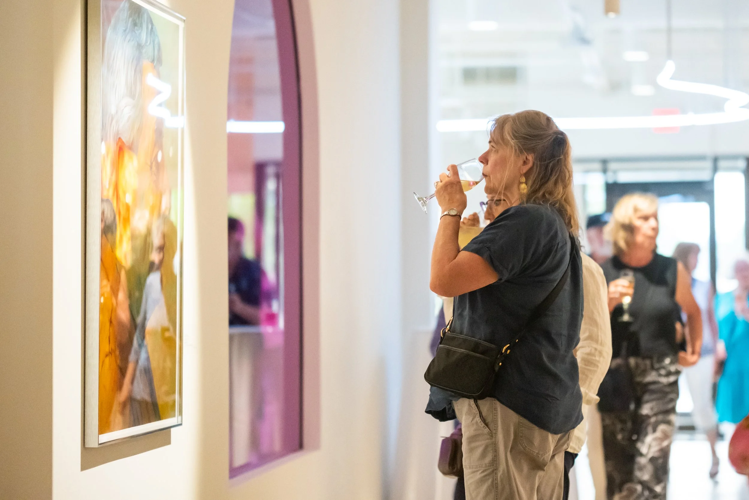 A person takes a sip of their drink while looking at artwork in the CAT's lobby. 