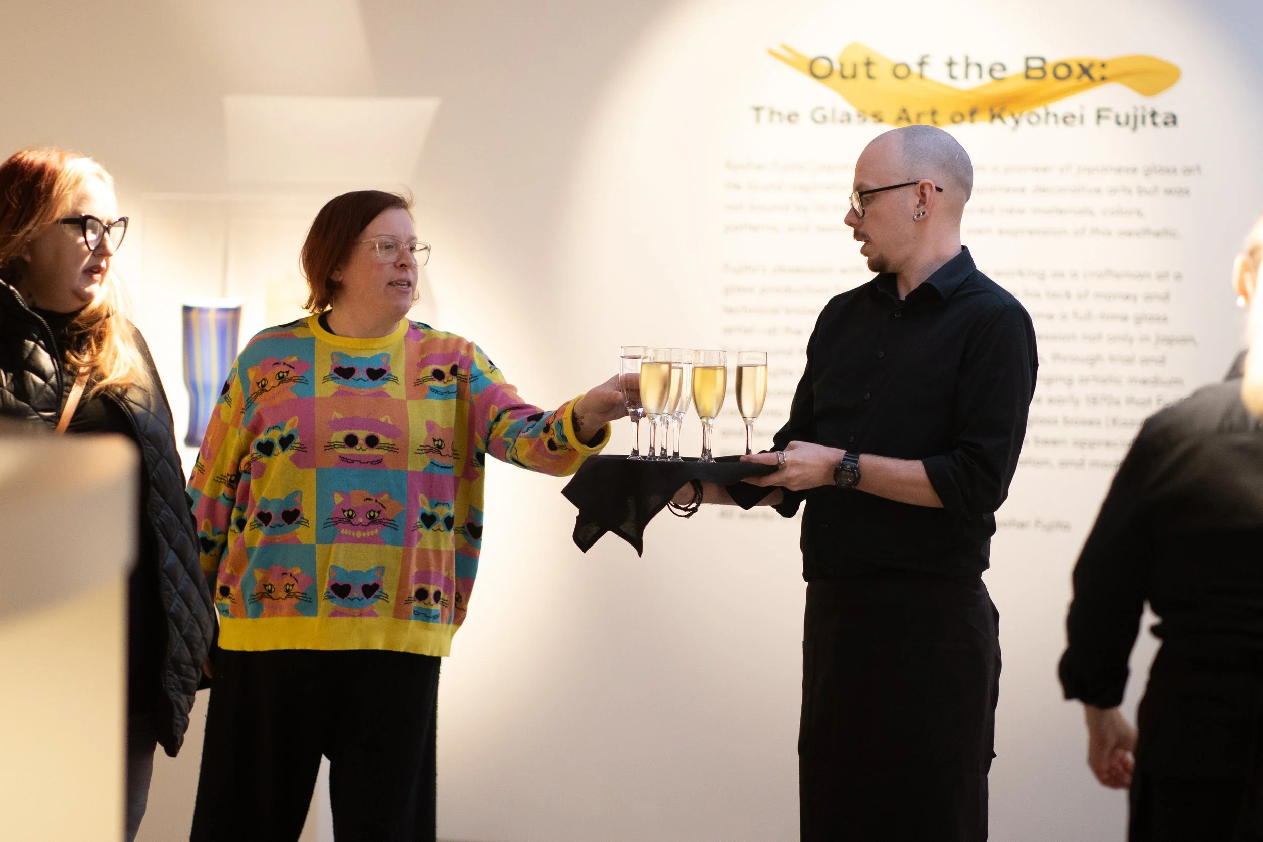 A waiter holds out a tray of glasses with champagne as a woman reaches to grab one. 