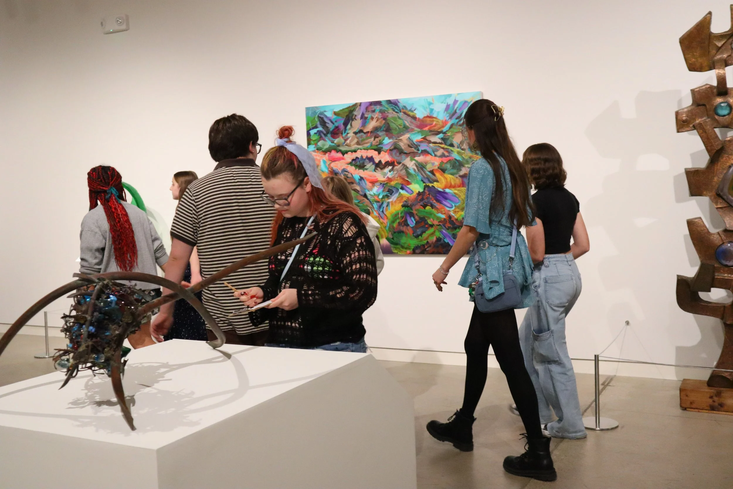 Teenagers moving through an exhibition while the central figure completes a scavenger hunt on a clipboard.