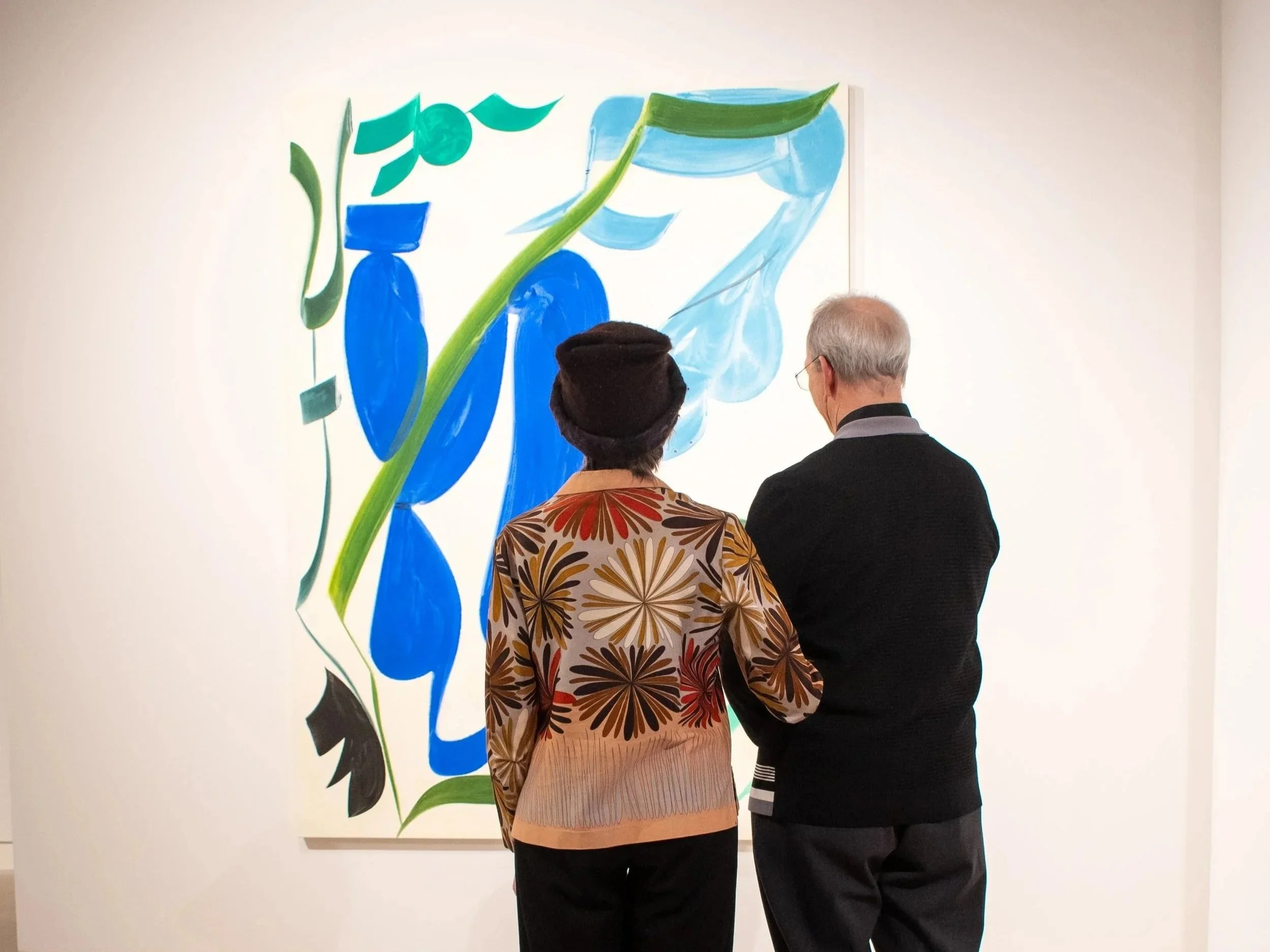 Two people, a woman and a man, are standing in front of a large abstract painting in an art gallery, viewing the artwork.