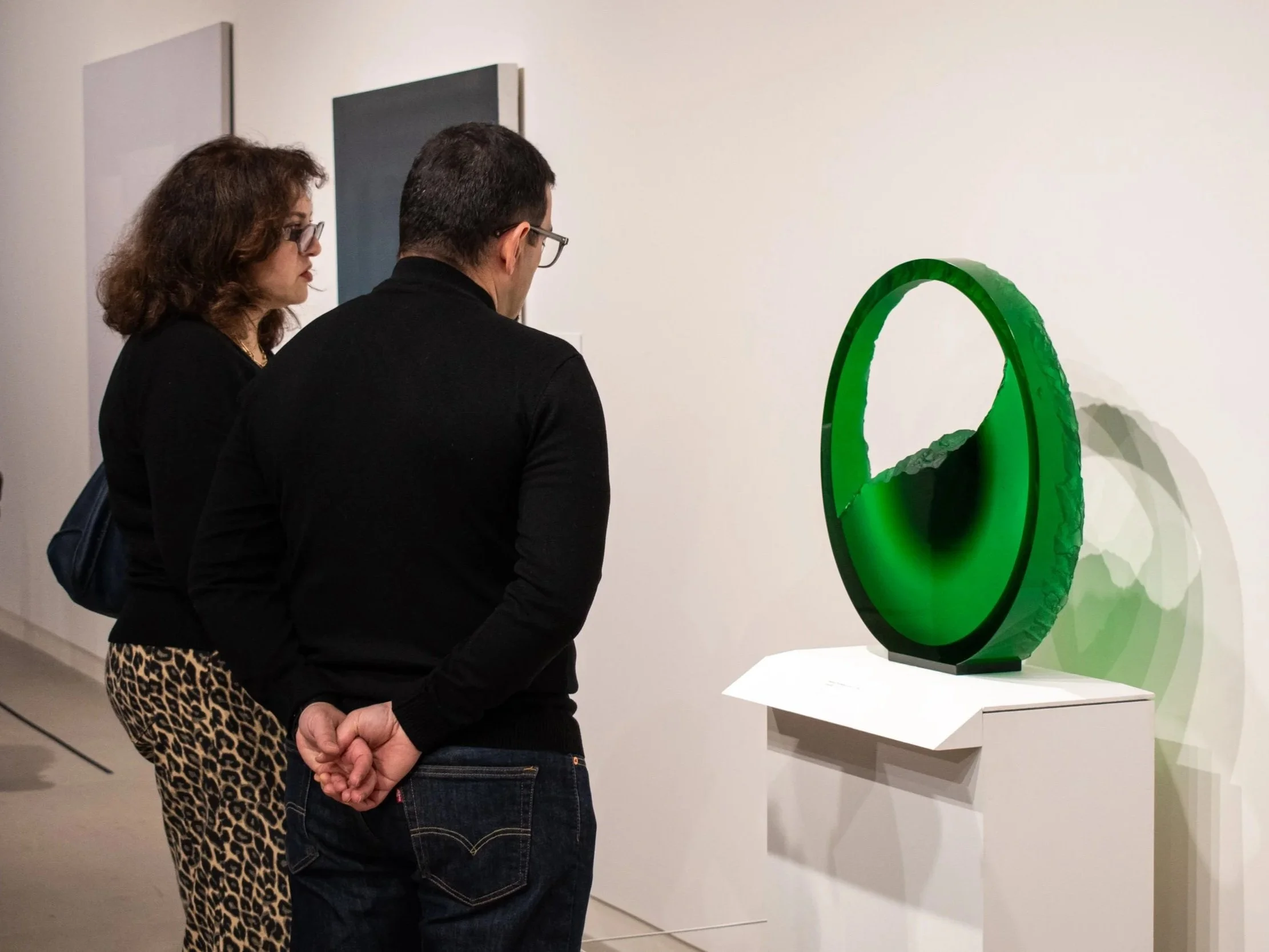 Two people observing a green sculpture with a mirror-like presence in an art gallery.