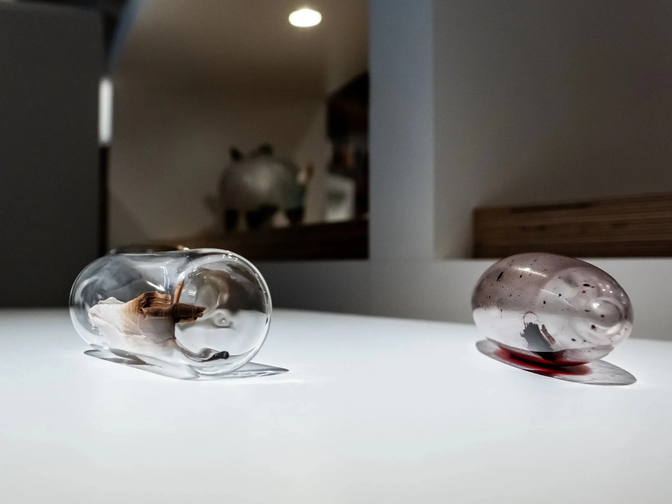 Close-up of two transparent decorative glass eggs on a white surface, with a blurred background of a kitchen or dining area.