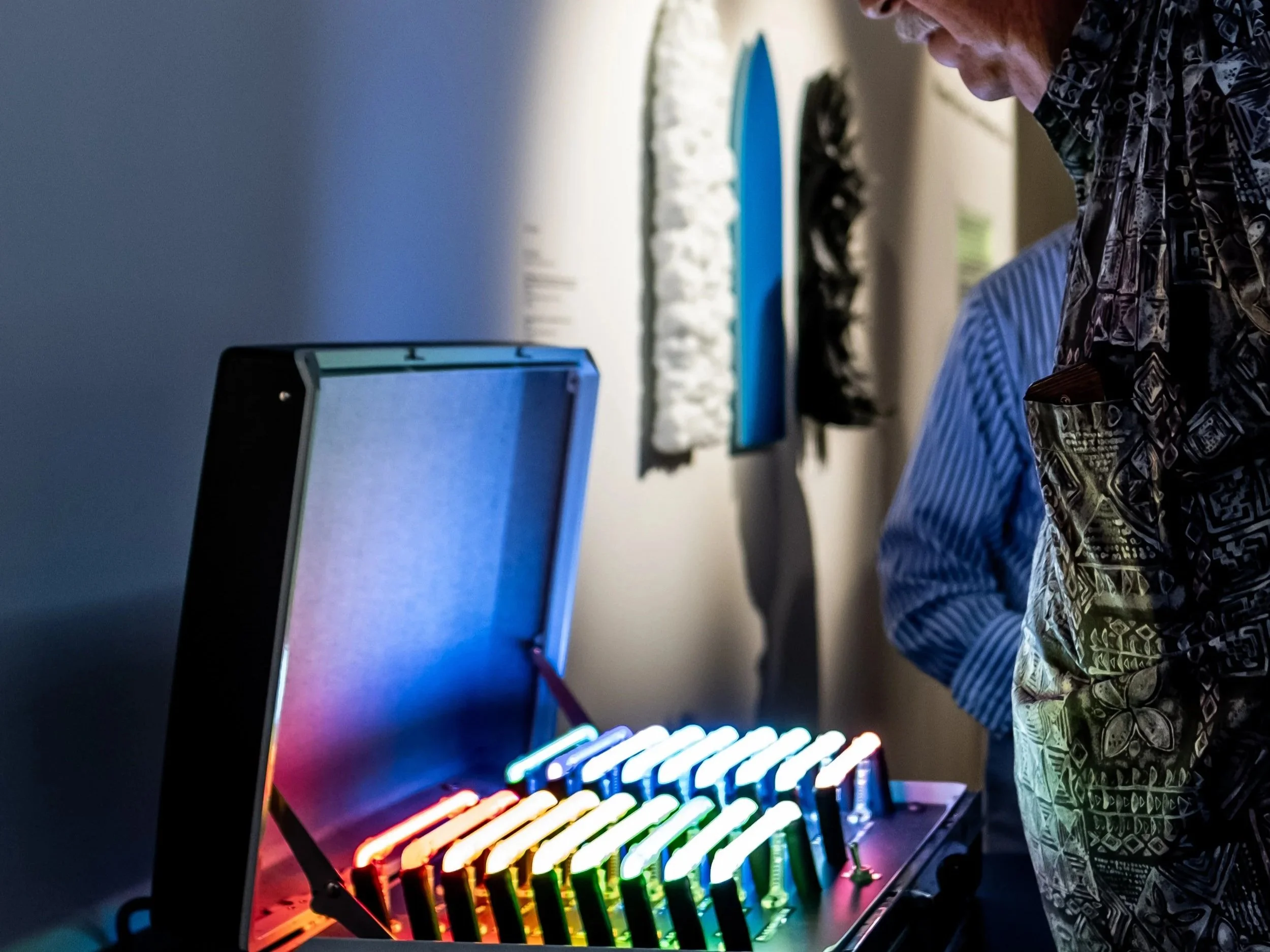 A person with a patterned shirt working on a laptop with a colorful LED rainbow keyboard.