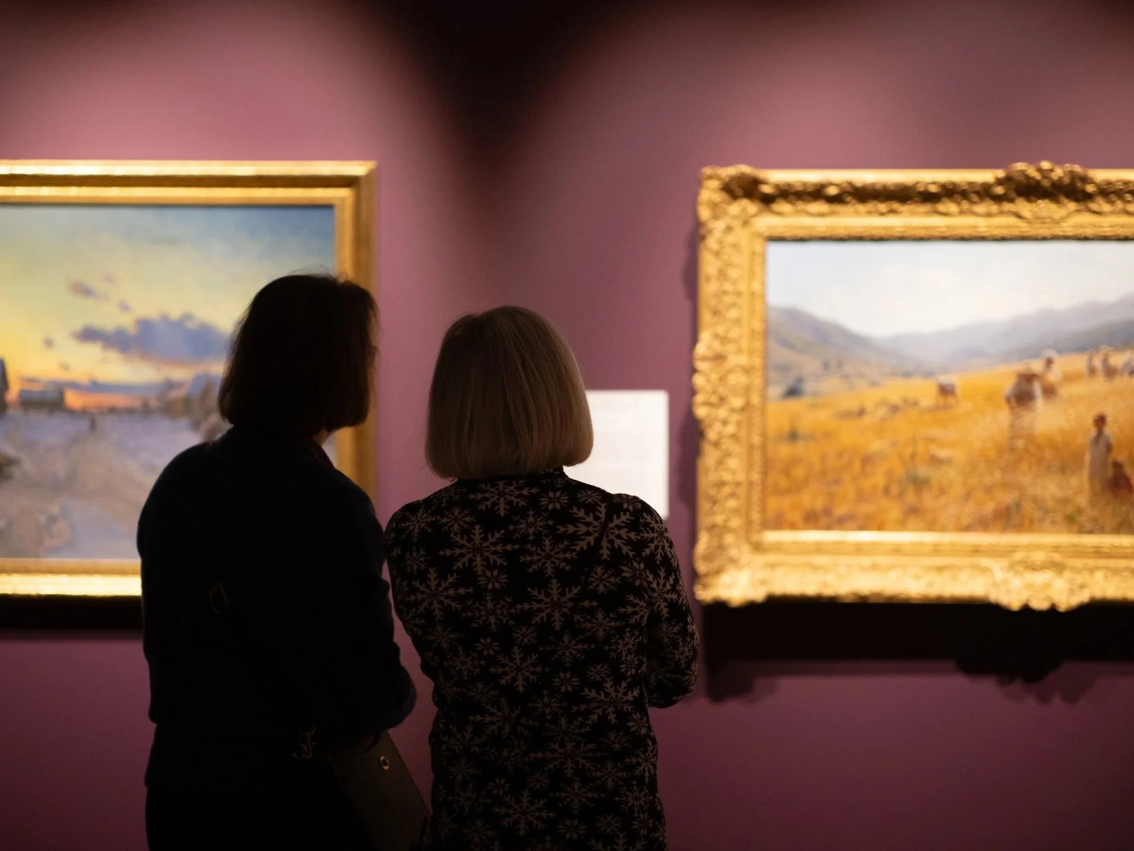Two women viewing paintings in an art gallery with purple walls.