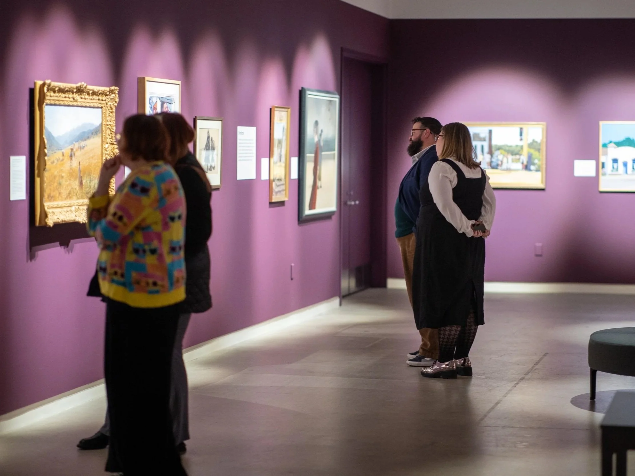 People observing paintings in a gallery with purple walls.