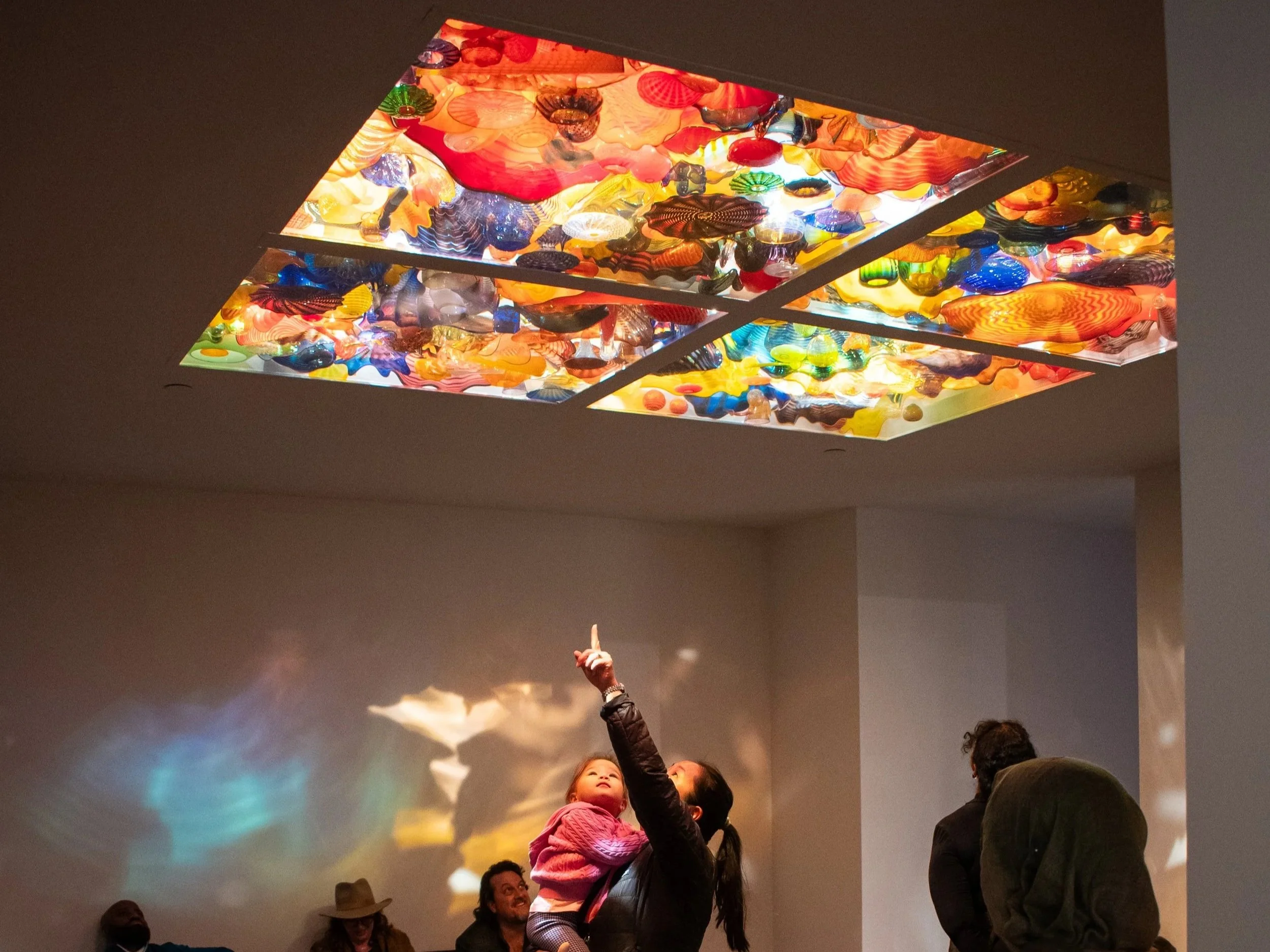 A mother and child looking up to a colorful glass ceiling.