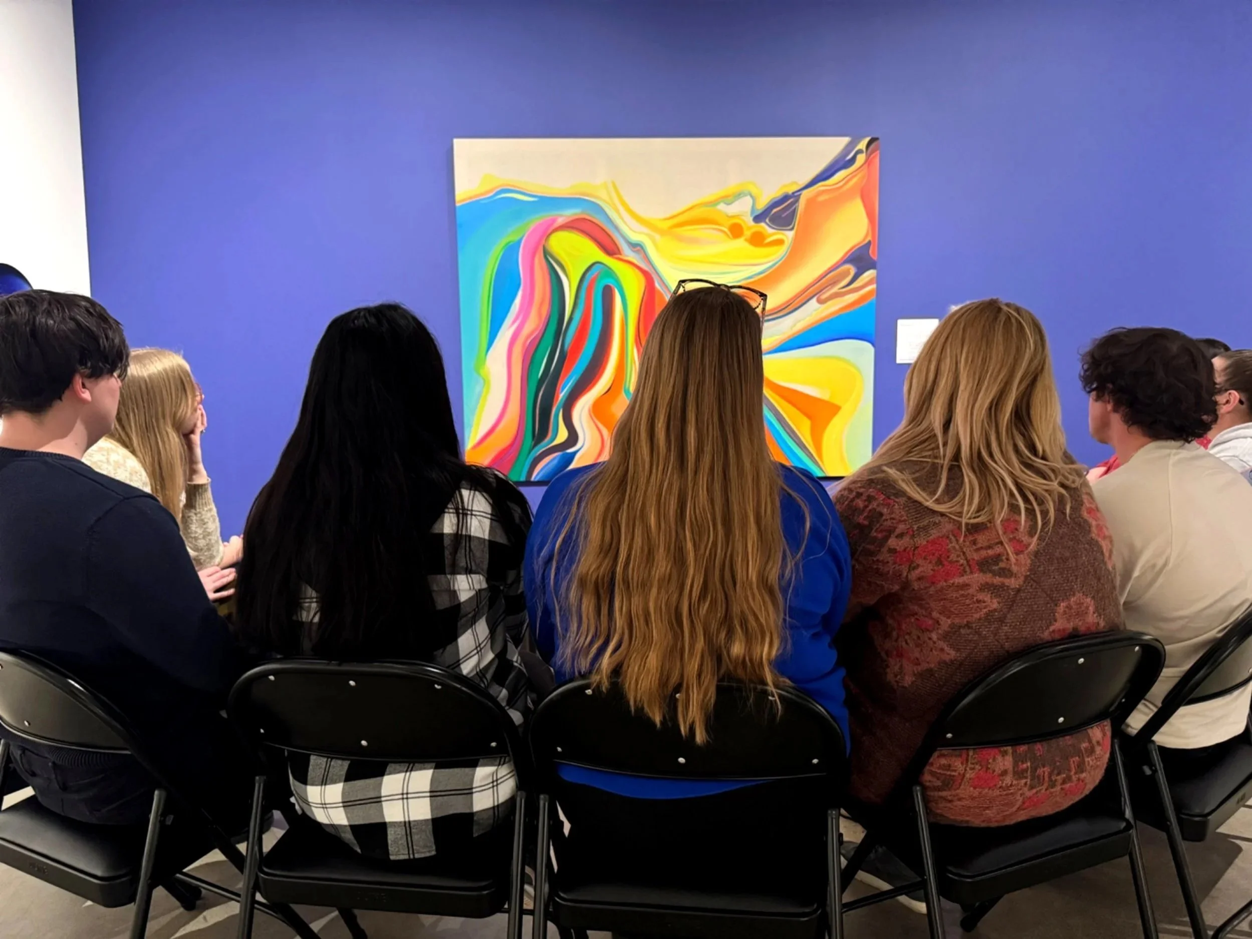 A group of seated adults in a semi-circle looking at a colorful abstract painting.