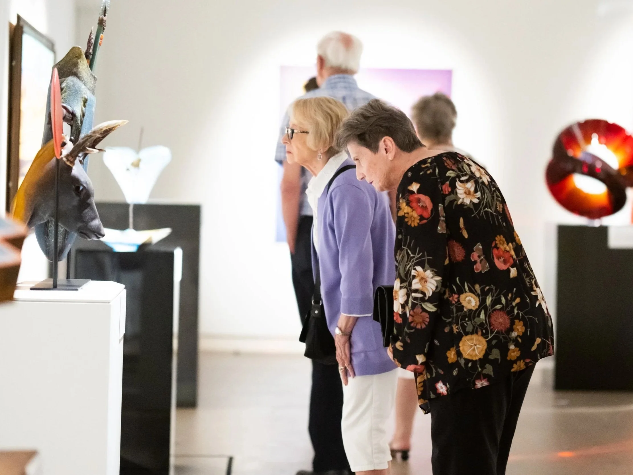 Two women leaning in to get a closer look at a sculpture in the gallery.