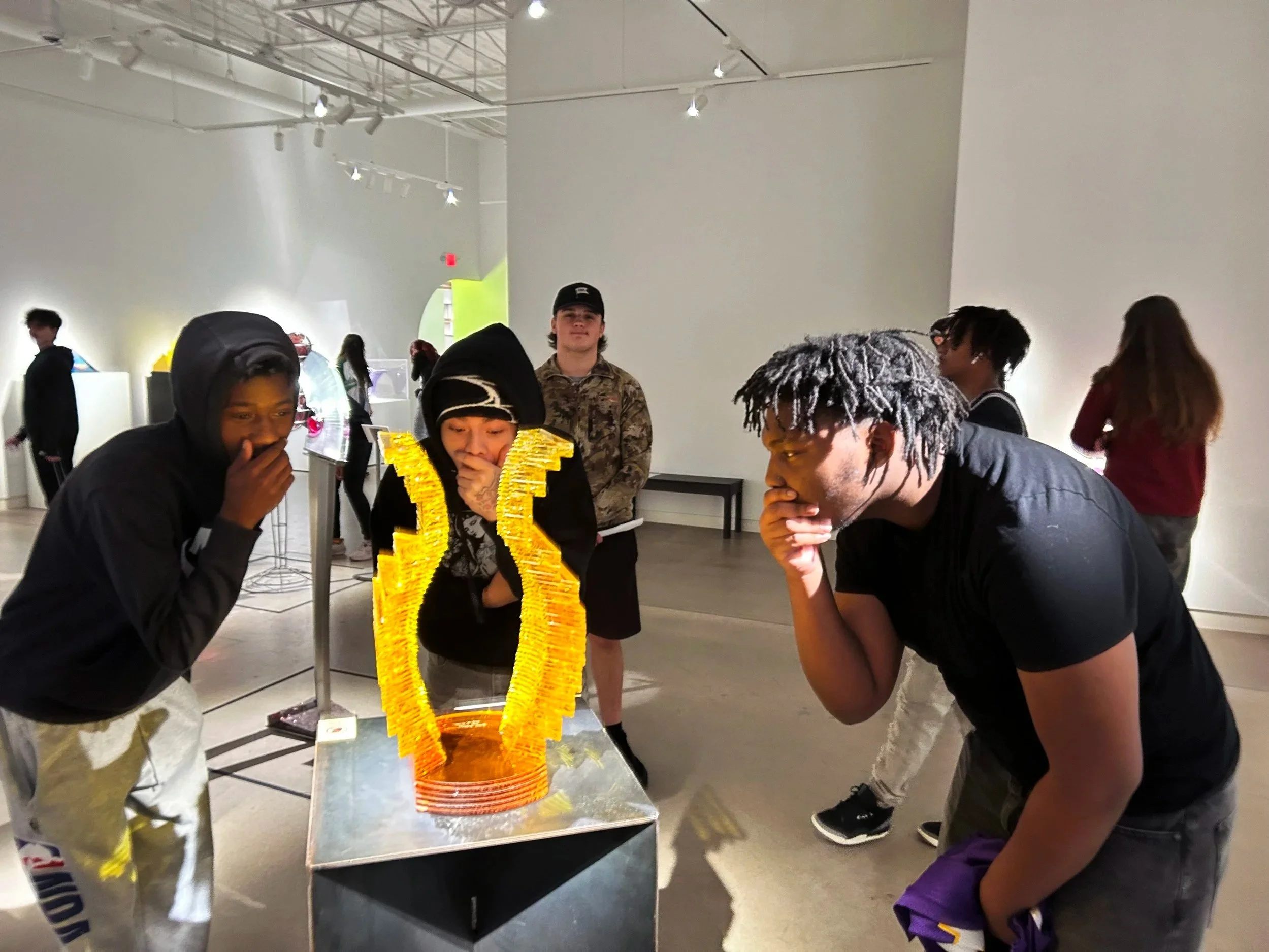 Three high school boys gathered around a sculpture making gestures of surprise.