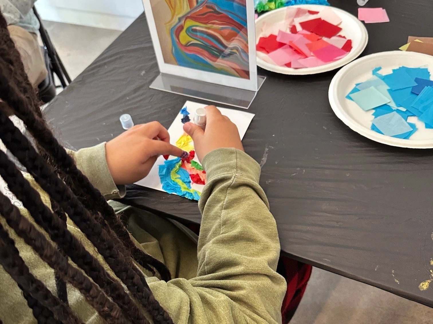 A student's hands making an abstract tissue paper collage.