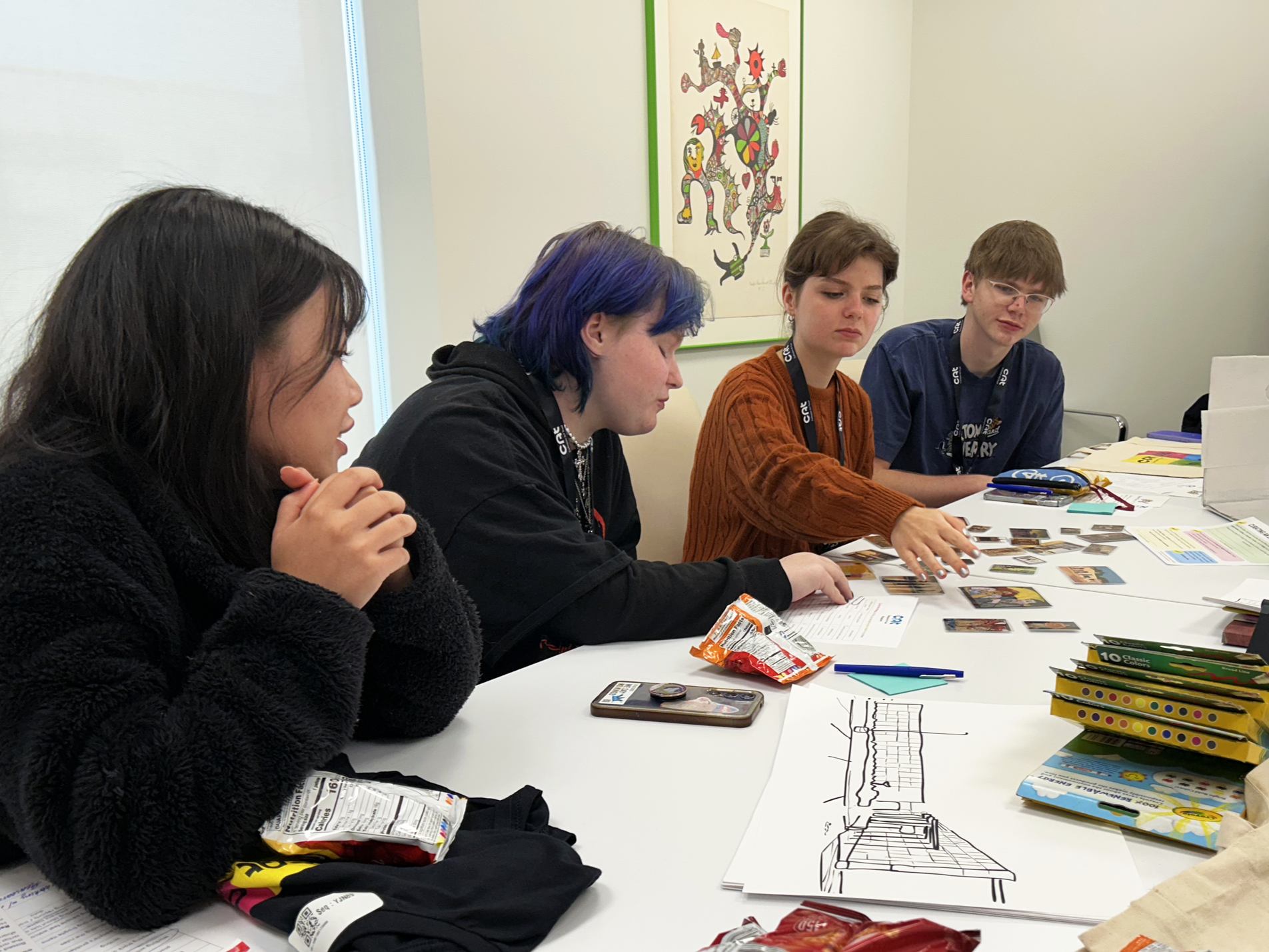 Four teenagers working together in a conference room to arrange miniature paintings on the table.