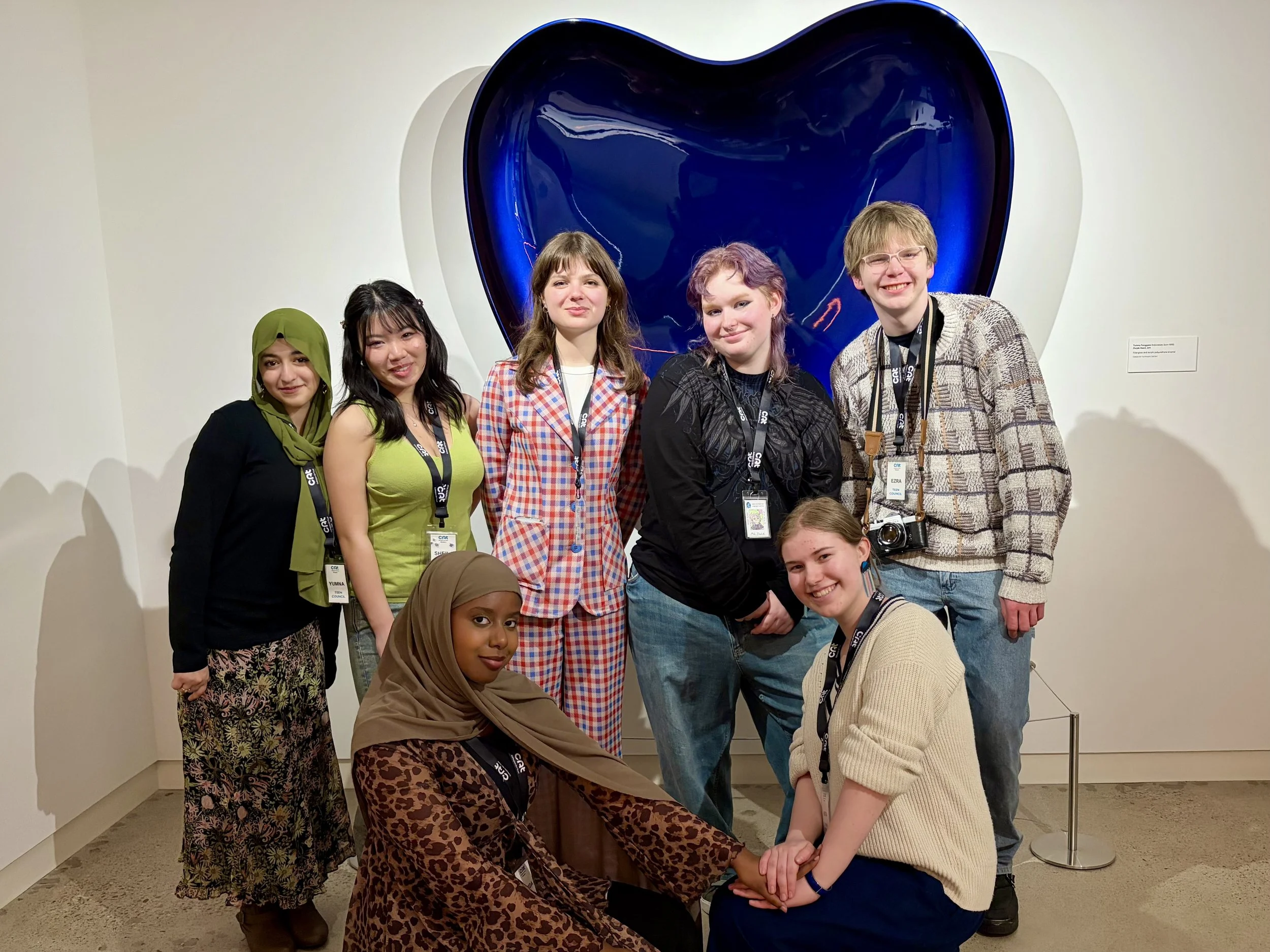  A group of teenagers pose together in front of a large purple heart sculpture.  