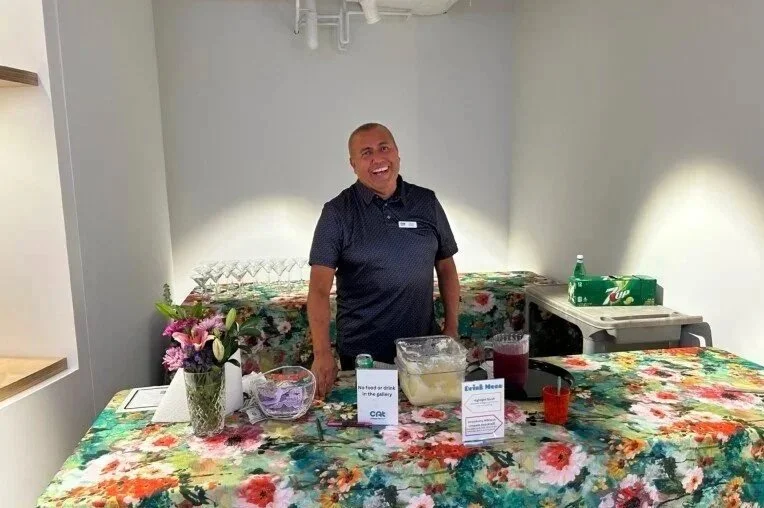 A person smiles while standing behind a bar with floral-patterned tablecloths. 