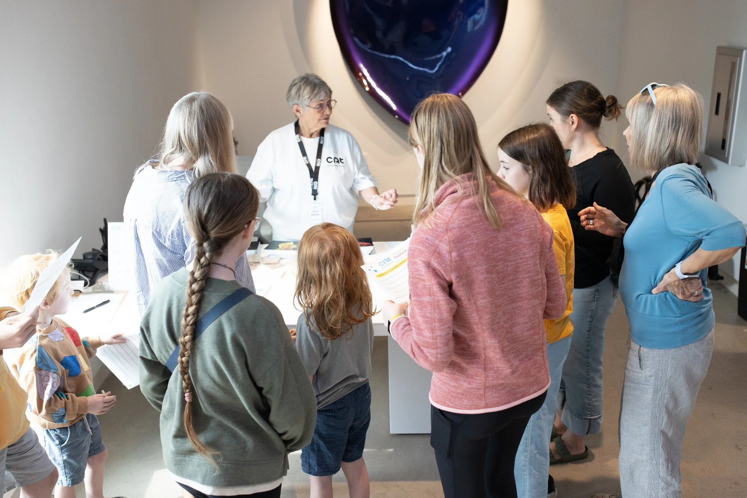 A museum volunteer engages a group of children standing around her.