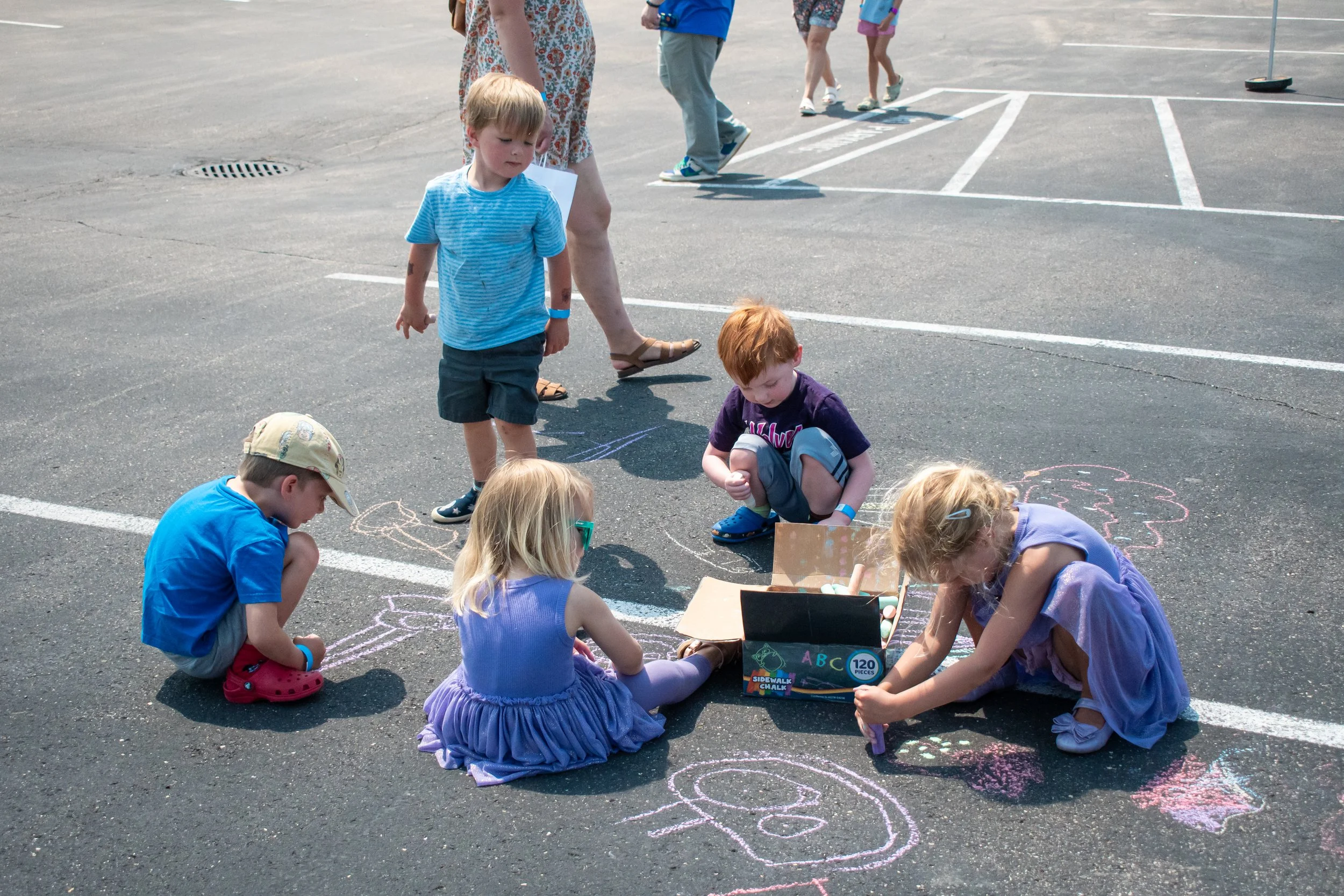 A group of children color on pavement with chalk. 