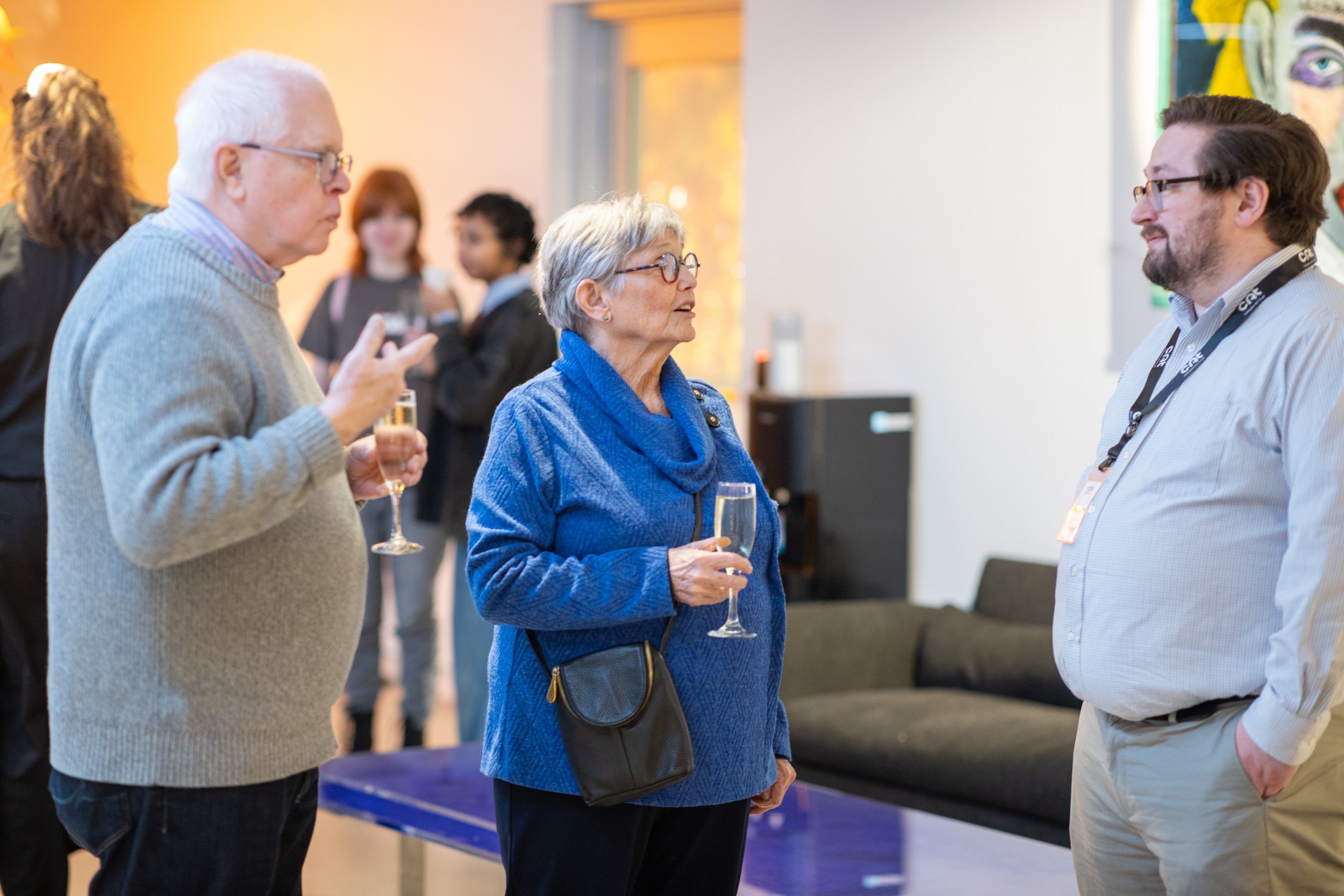 Three adults converse while holding champagne glasses. 