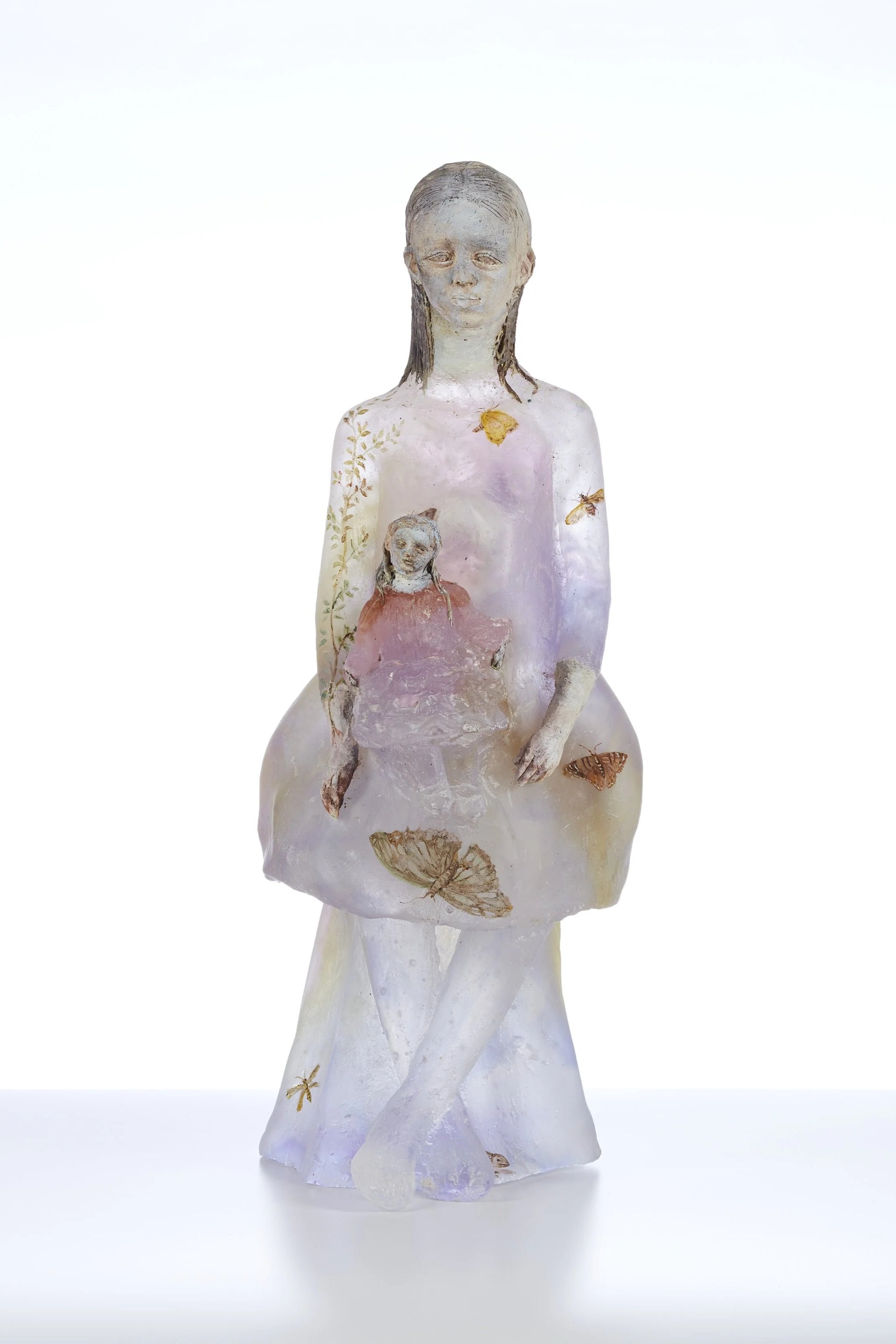 A statue of a woman with closed eyes holding a small child, decorated with butterflies and floral patterns. The statue has a soft, translucent appearance.