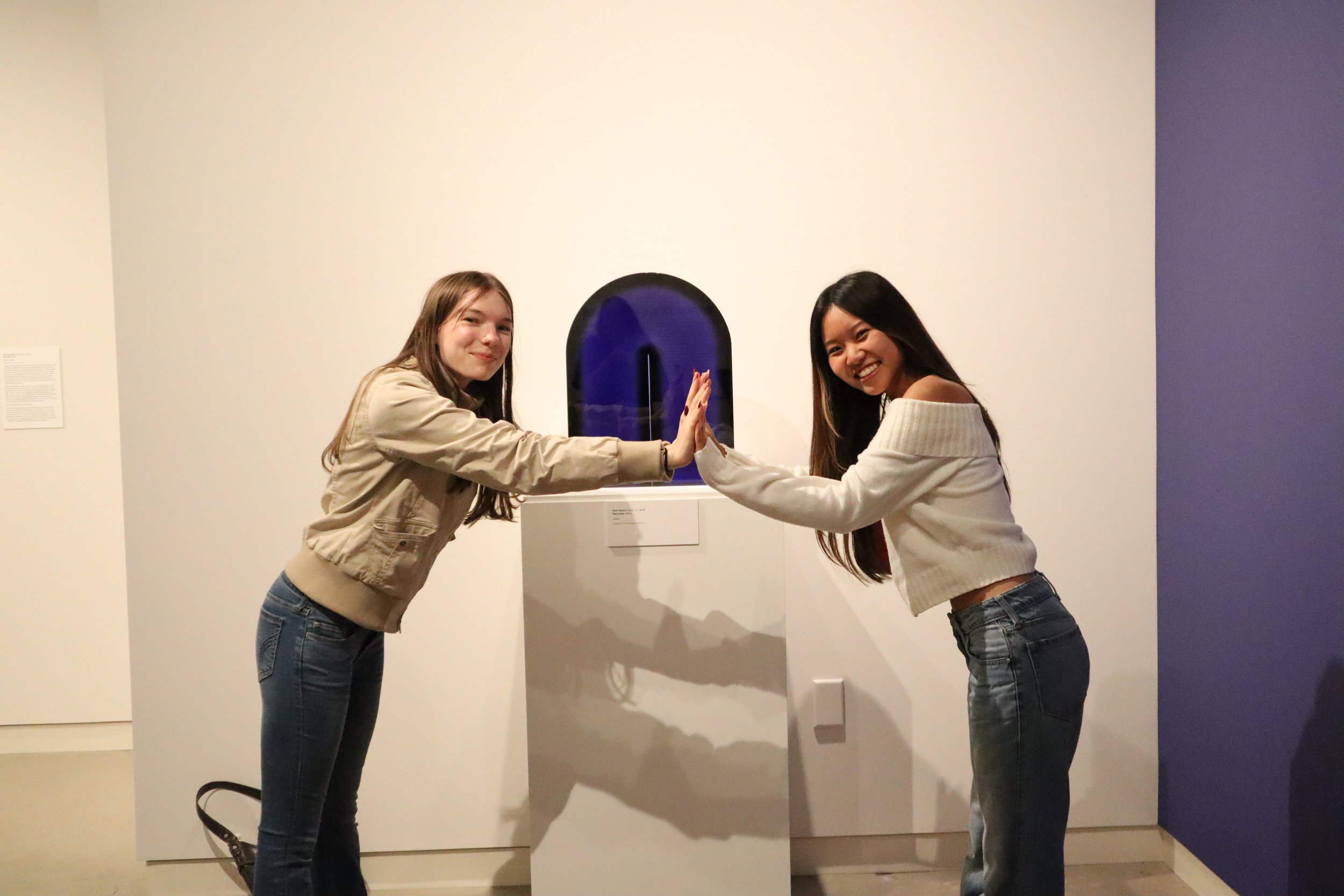 Two teenagers high-fiving in front of a blue glass sculpture.