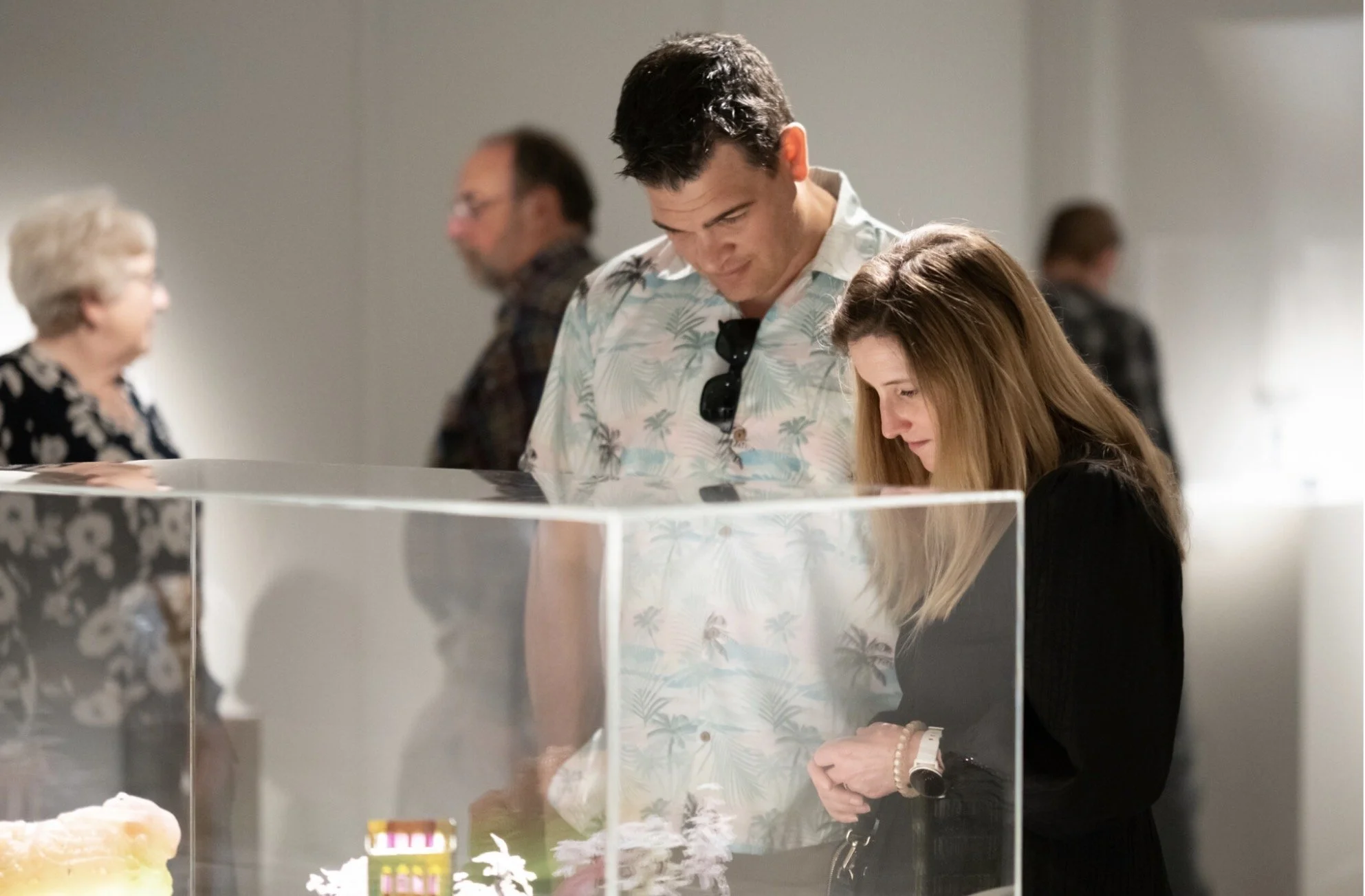 Visitors in the gallery studying sculpture inside a case.