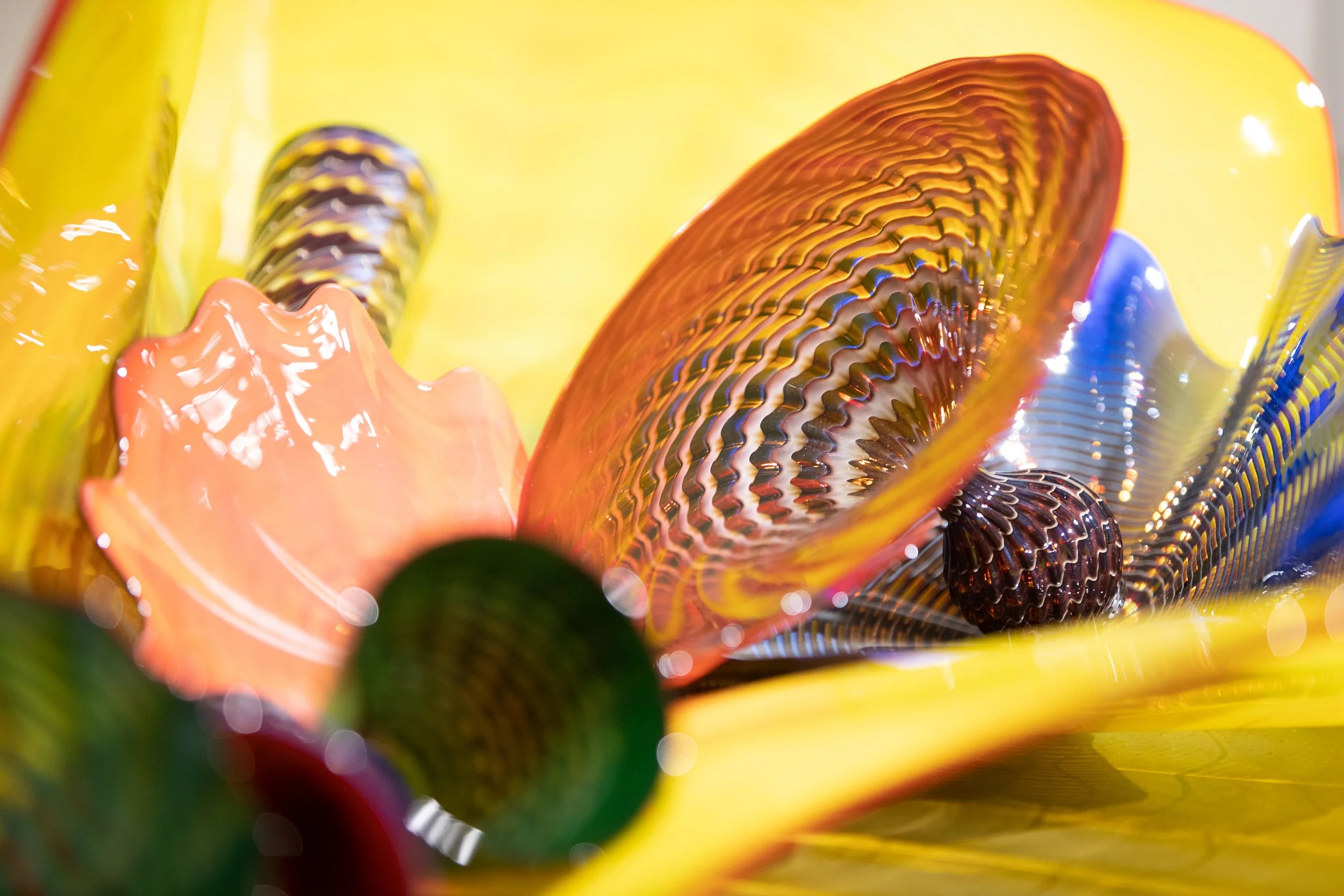 Close-up of colorful glass art with vibrant yellow, orange, blue, and green glass pieces featuring intricate patterns and textures.