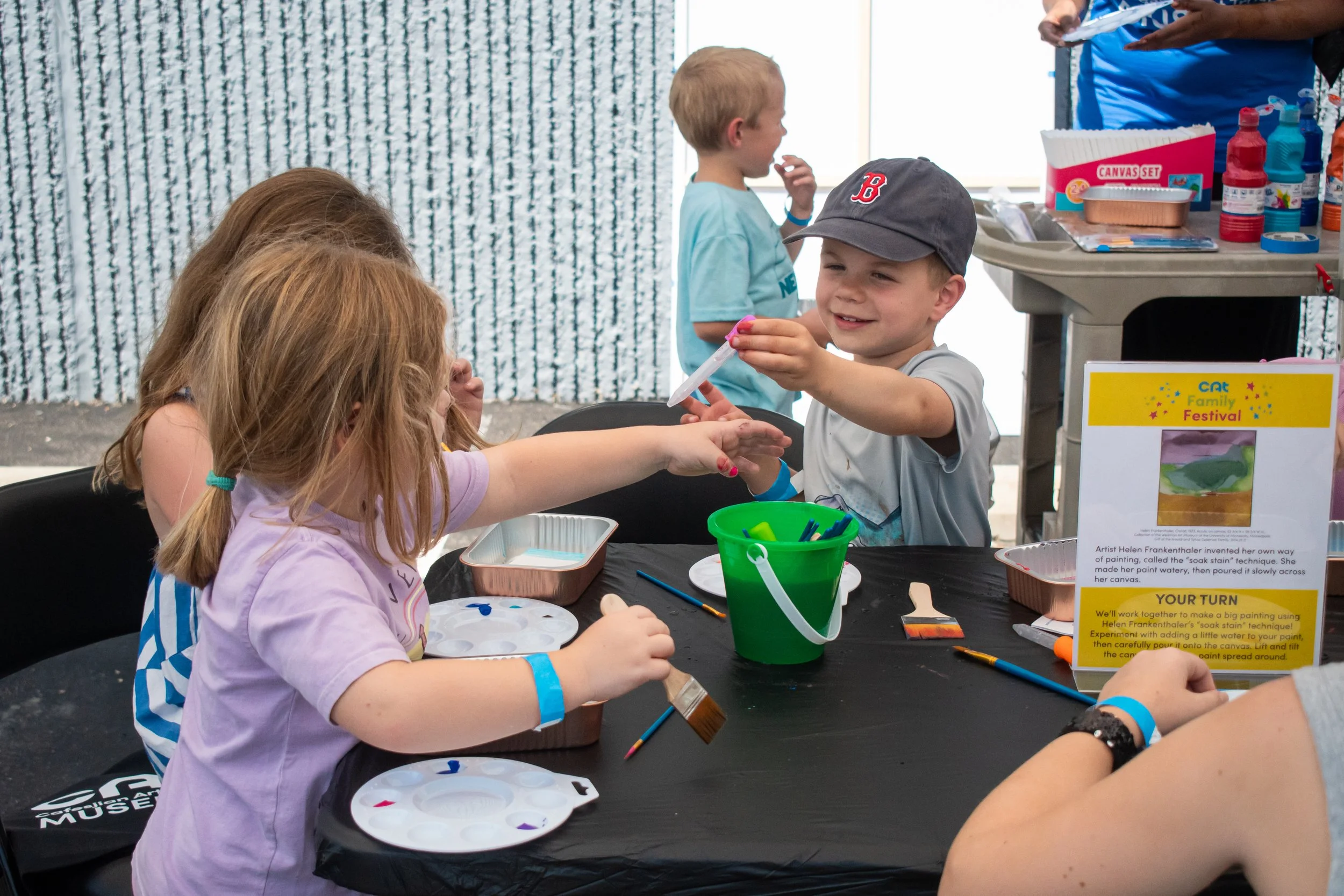 A group of children gathering around a table, holding paintbrushes and eyedroppers. 