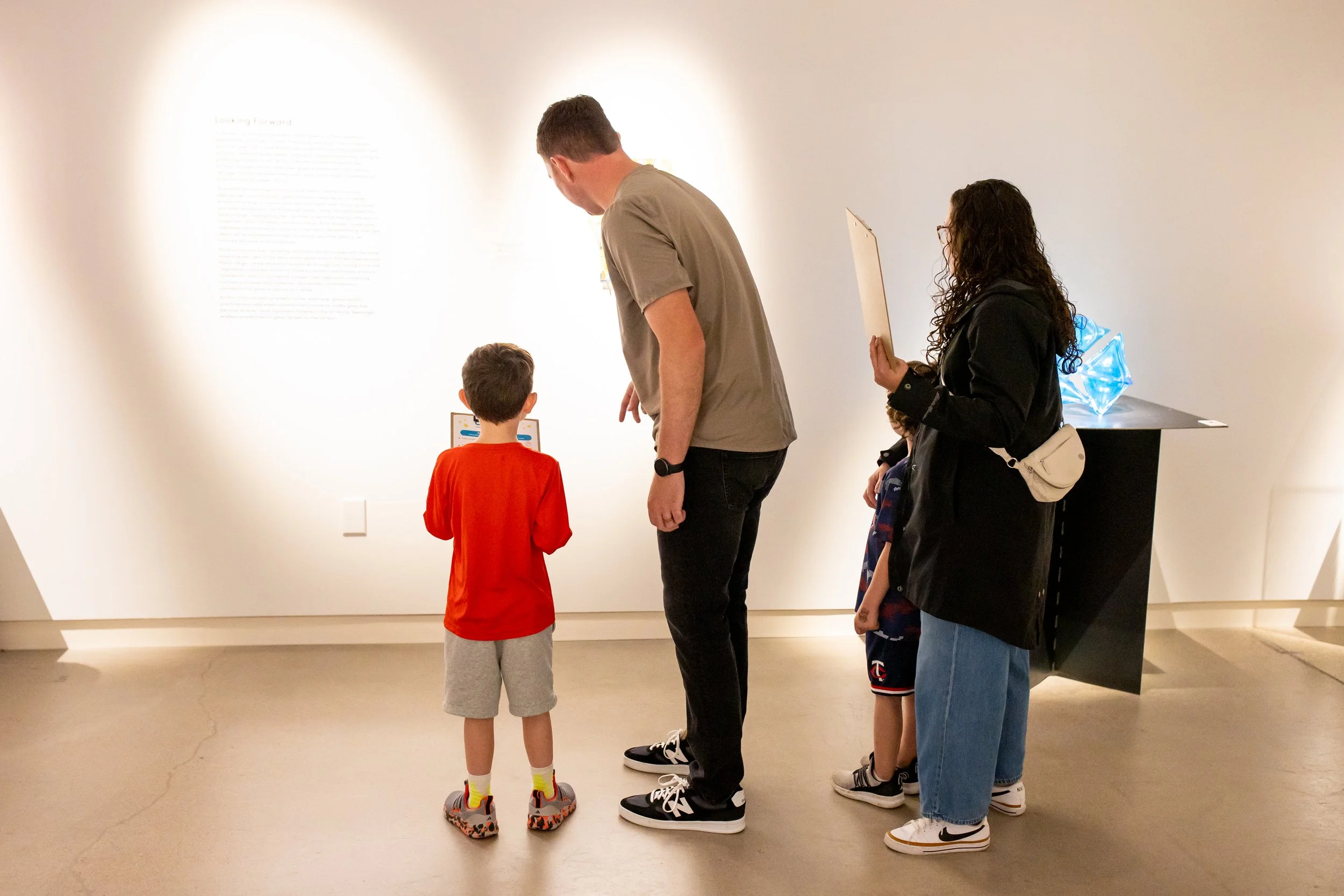 An adult points to something in a gallery, two children and another adult stand by him. 